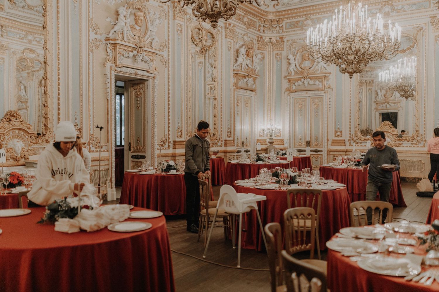 Elegant baroque dining room with crystal chandeliers and round tables with red tablecloths.