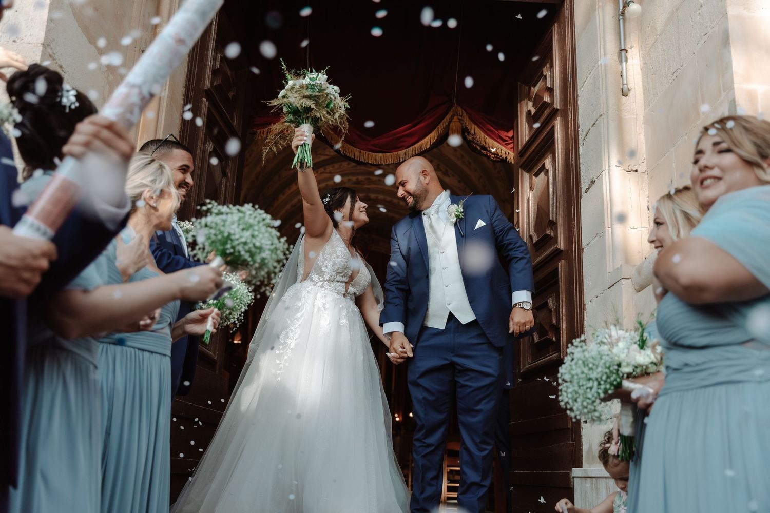 Newlyweds celebrate with joy as they exit their wedding ceremony while guests shower them with confetti.