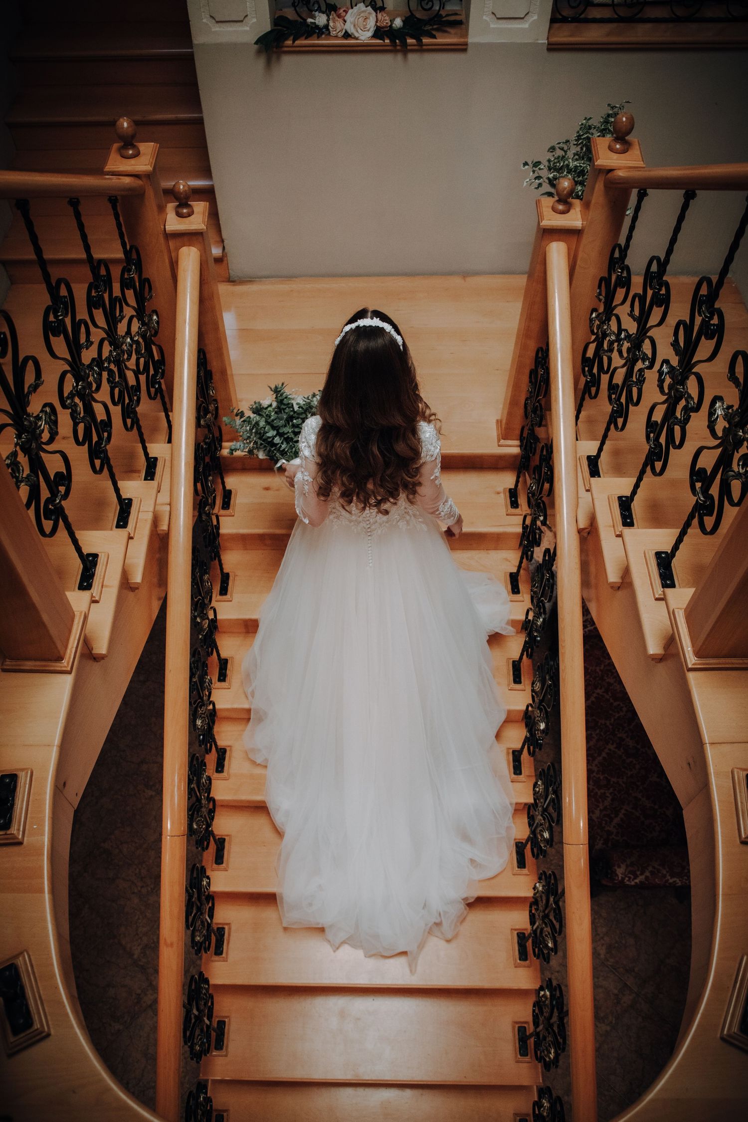 White wedding dress flowing down elegant wooden stairs with ornate black iron railings.