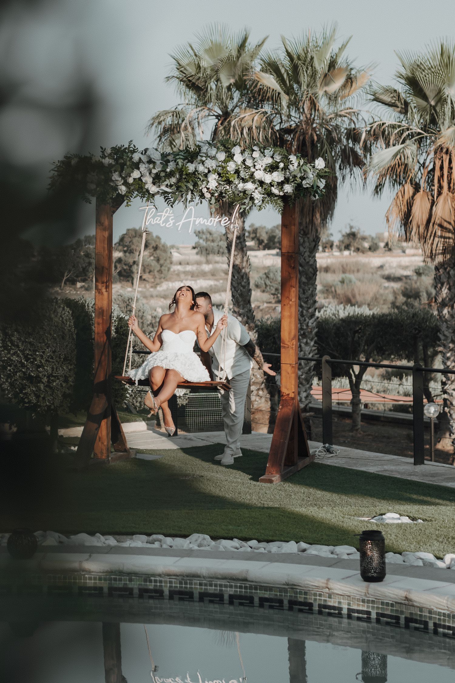 Scenic wedding venue with wooden pergola and poolside tropical landscaping.