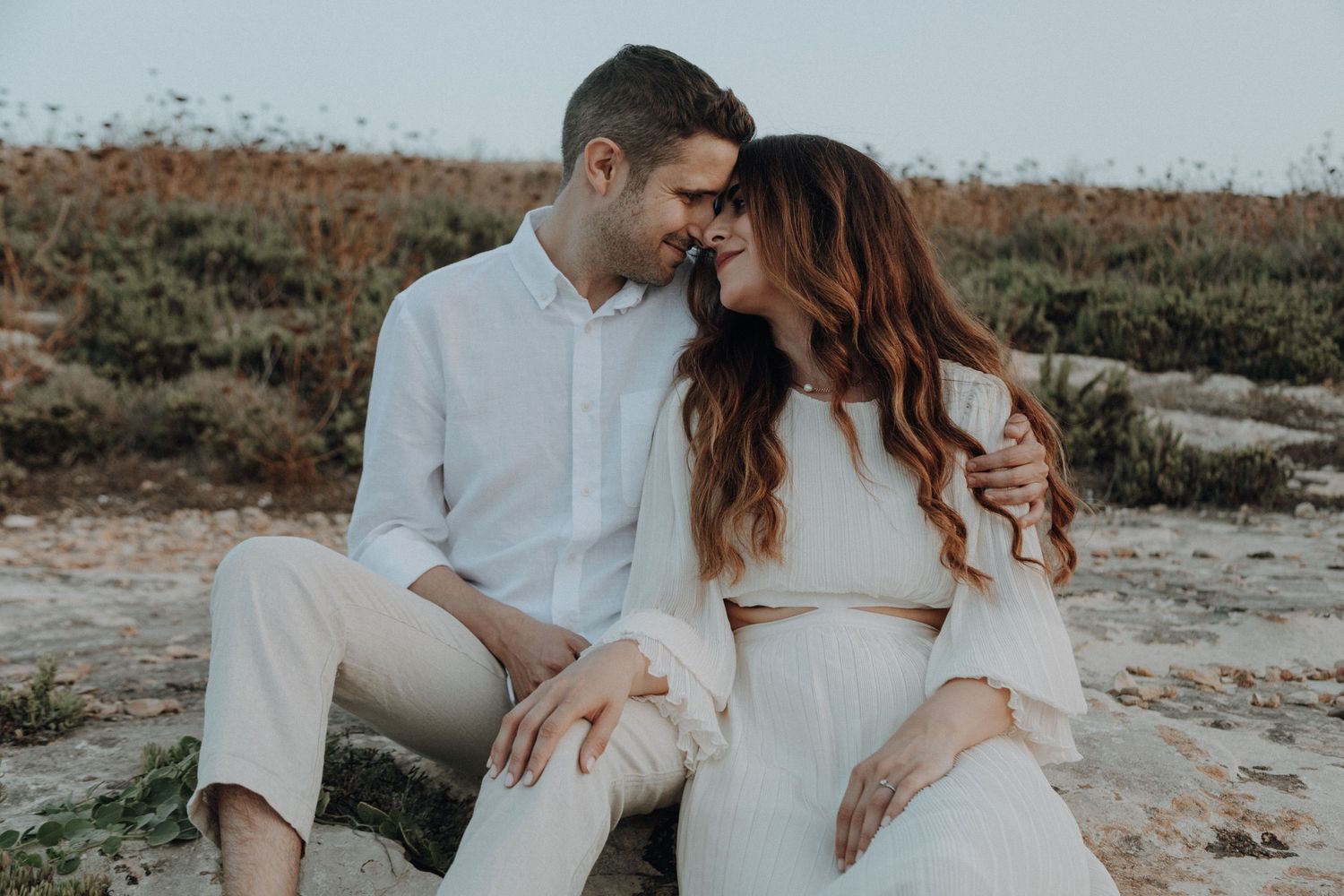 Intimate coastal photoshoot of a couple in white clothing at sunset.