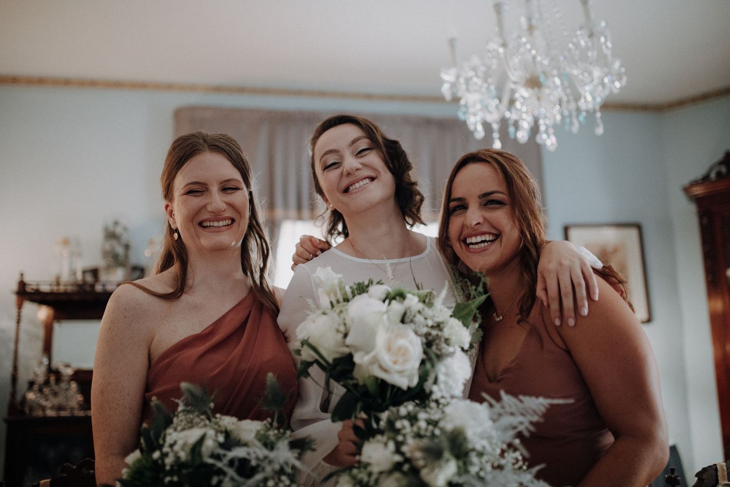 Wedding party smiles together while holding white and green floral arrangements.