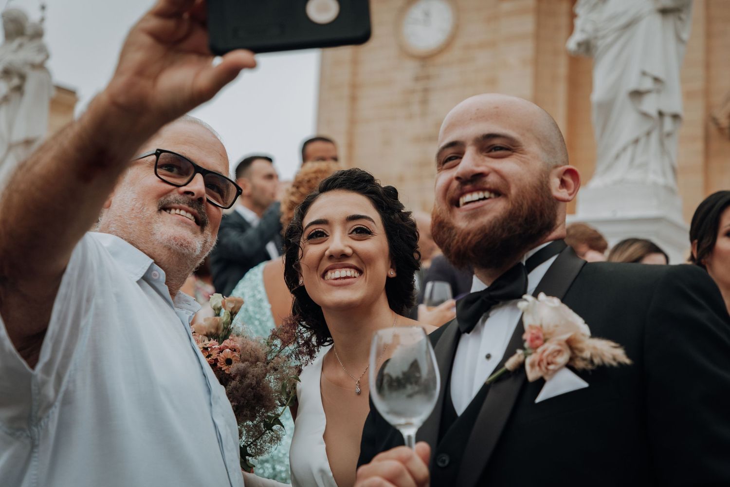Wedding celebration guests taking selfies and sharing drinks during the outdoor reception.