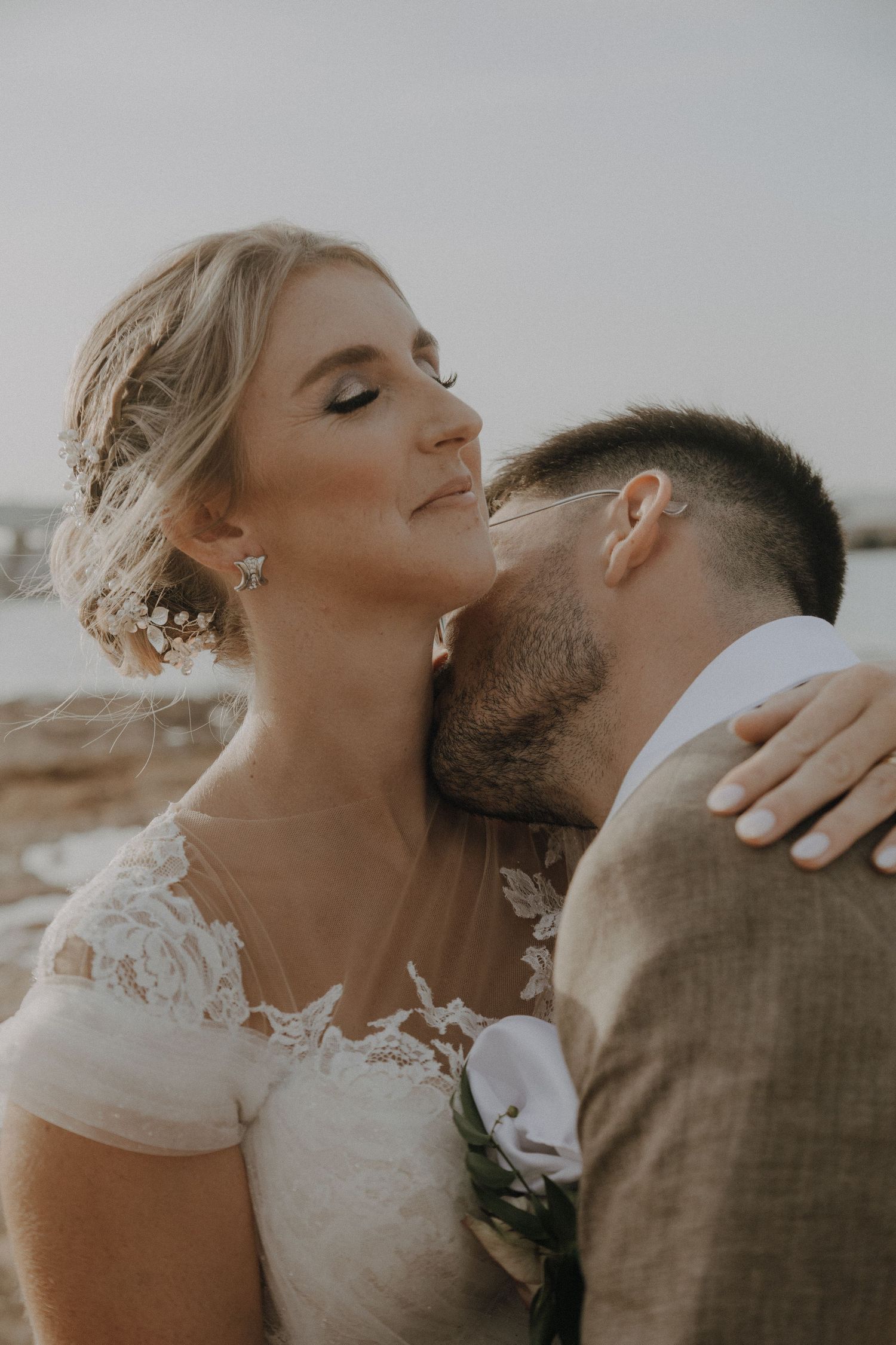 Tender wedding moment captured in muted tones against coastal scenery.