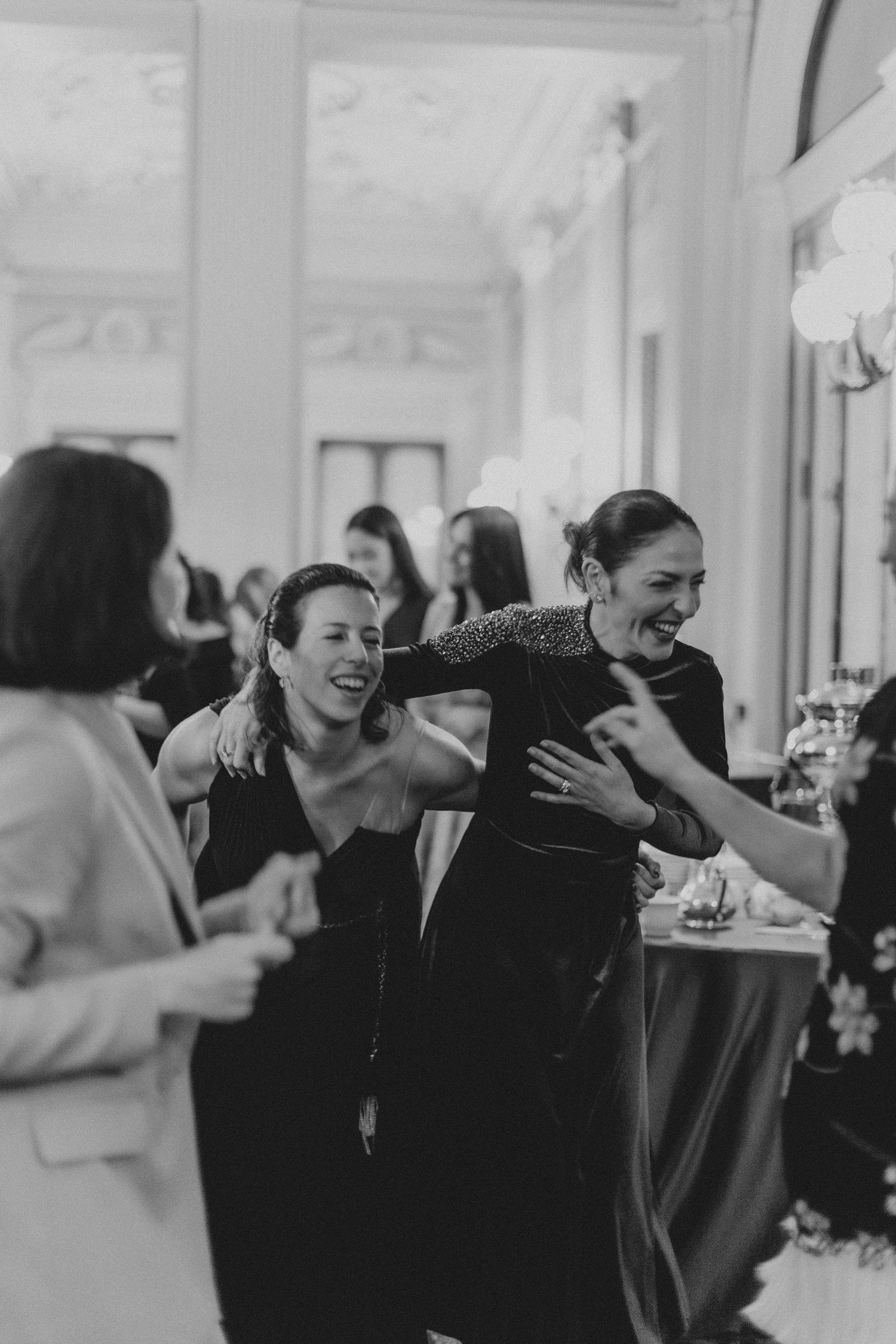 Women laughing and embracing at a joyful celebration in an elegant venue.