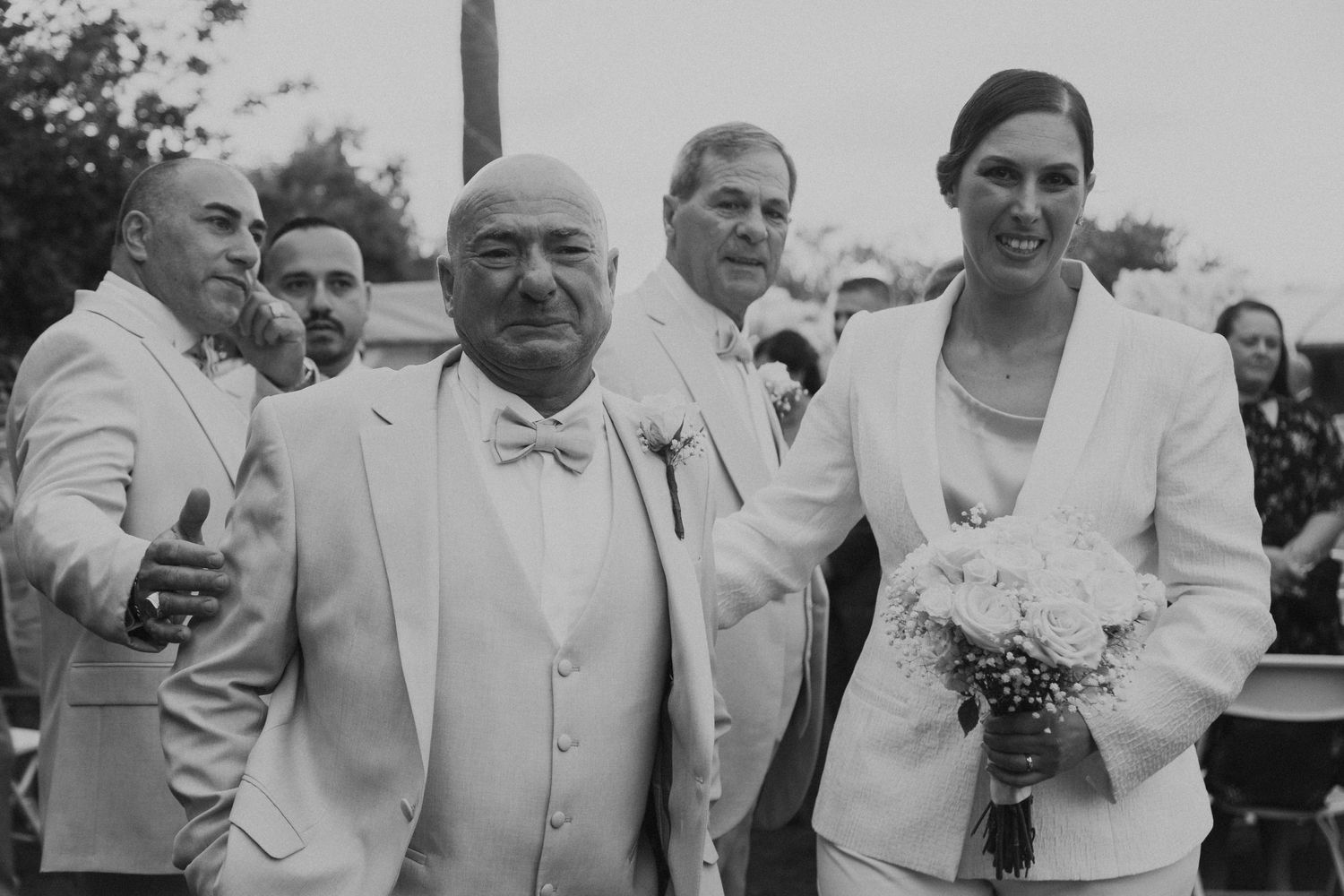 Black and white vintage-style wedding photo of guests in formal attire at outdoor celebration.