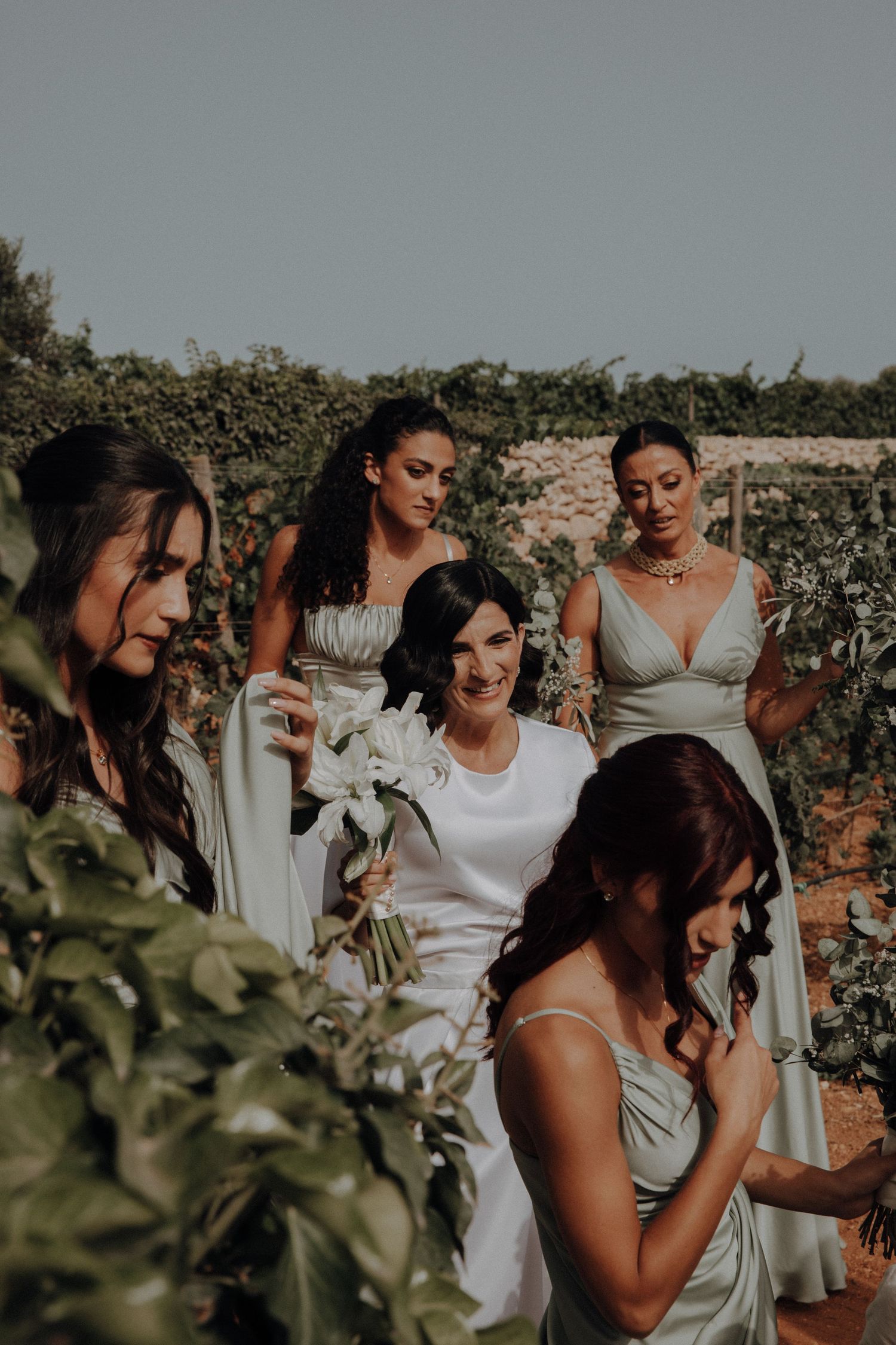 A bridal party in elegant silk dresses poses together in a garden setting.