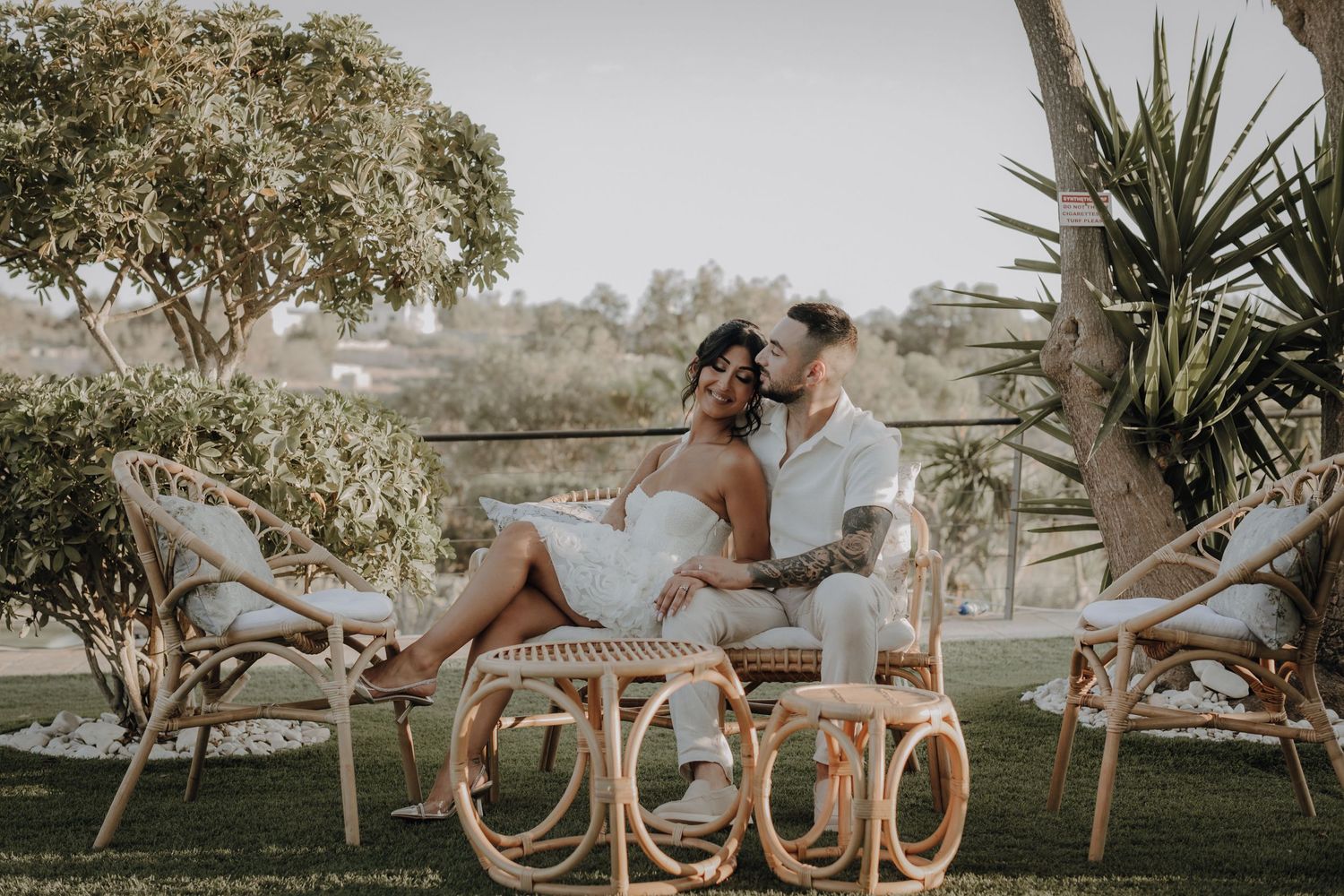 A romantic couple lounges in rattan chairs during an outdoor wedding photoshoot.