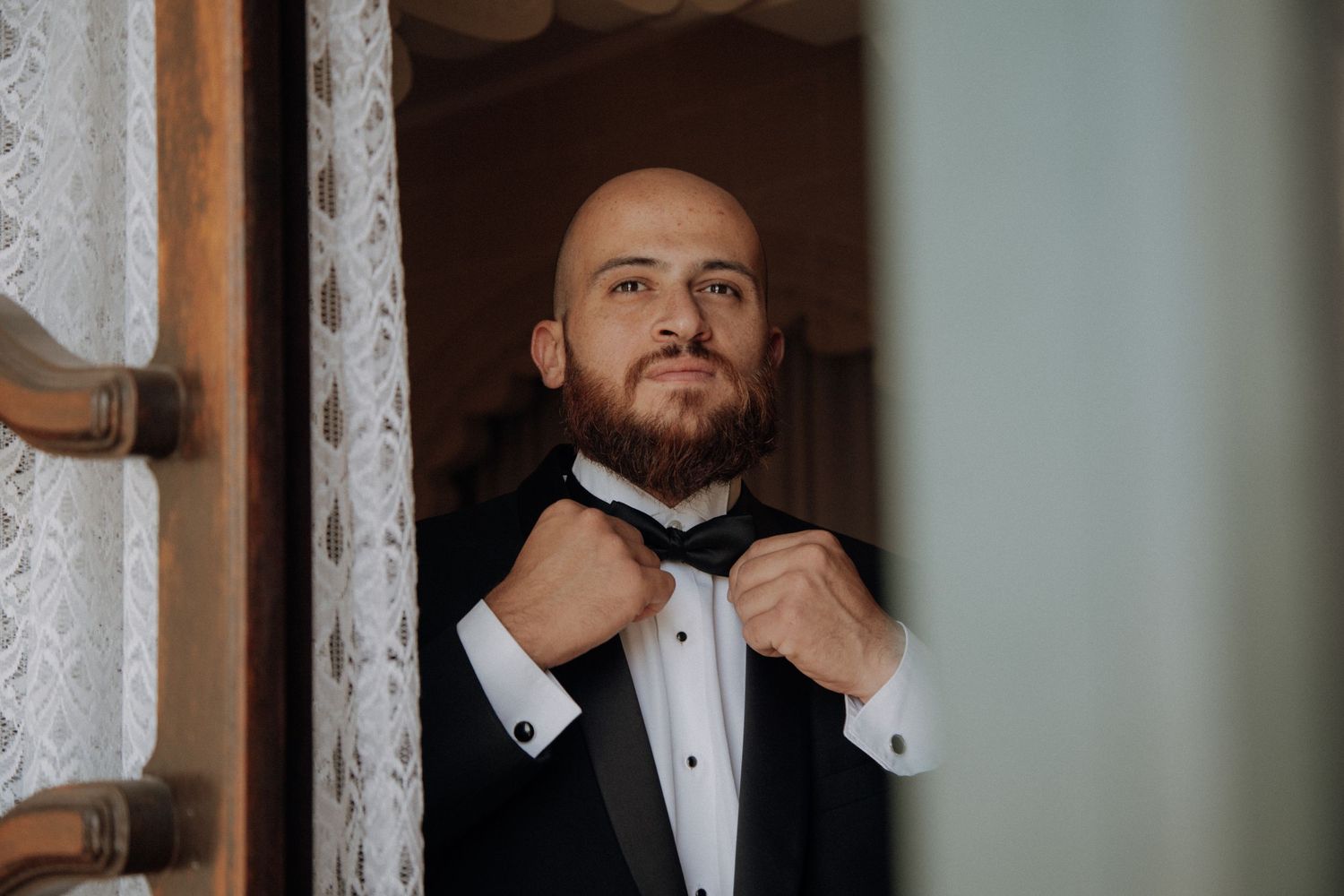 Person adjusting formal bow tie in mirror reflection.