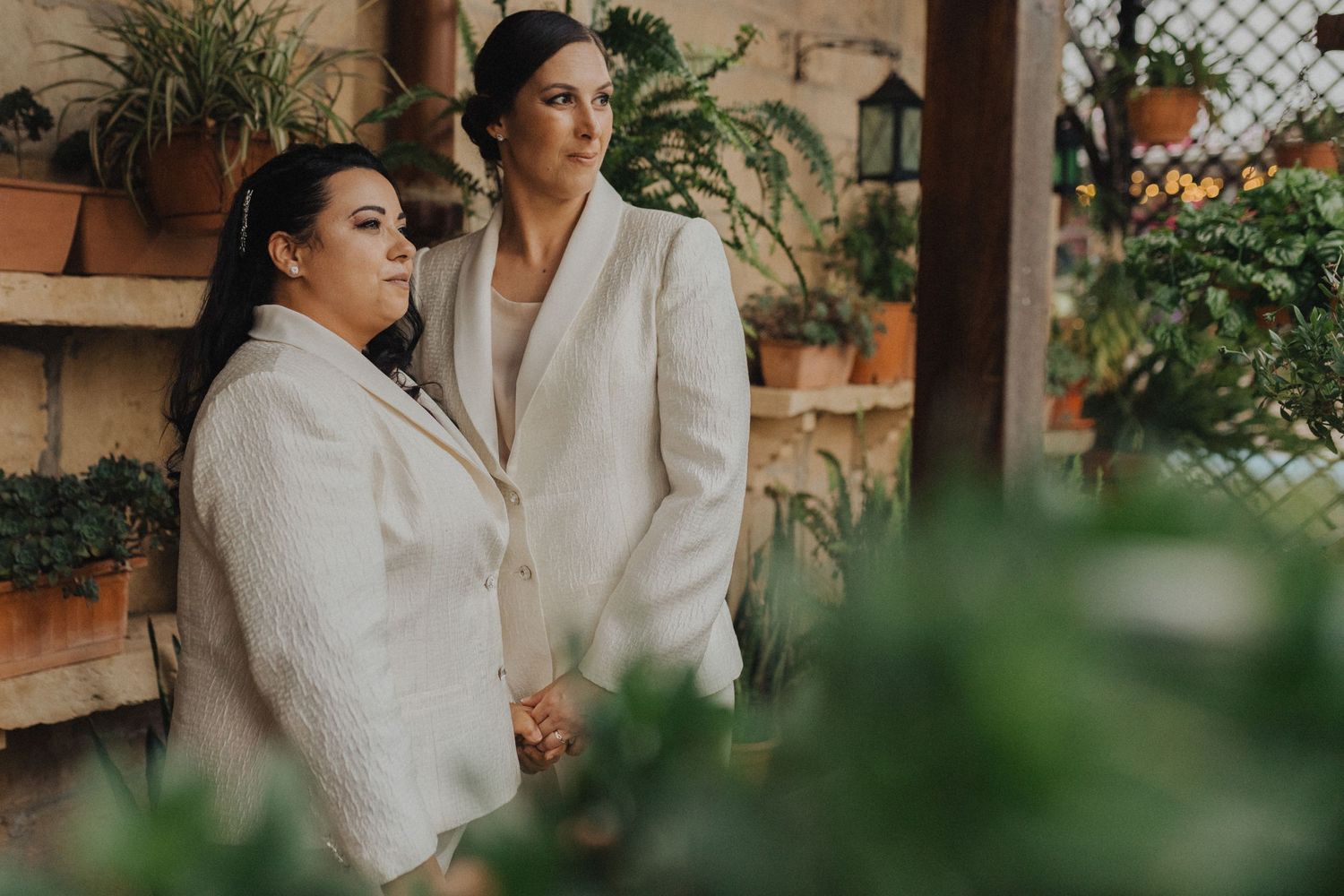 Two people wearing elegant white blazers stand together in a romantic garden setting.
