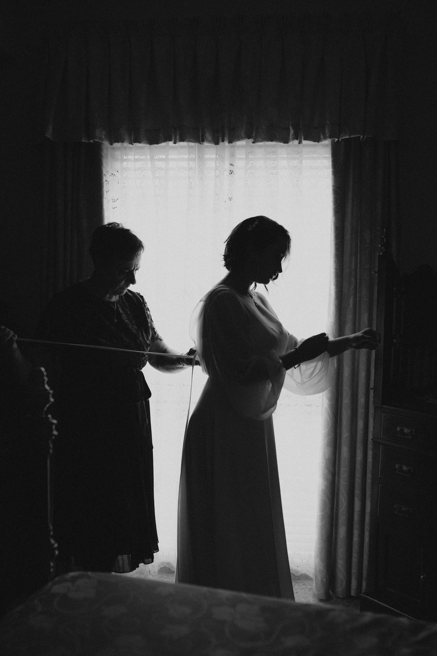 Silhouettes against window light create dramatic wedding day preparation scene.