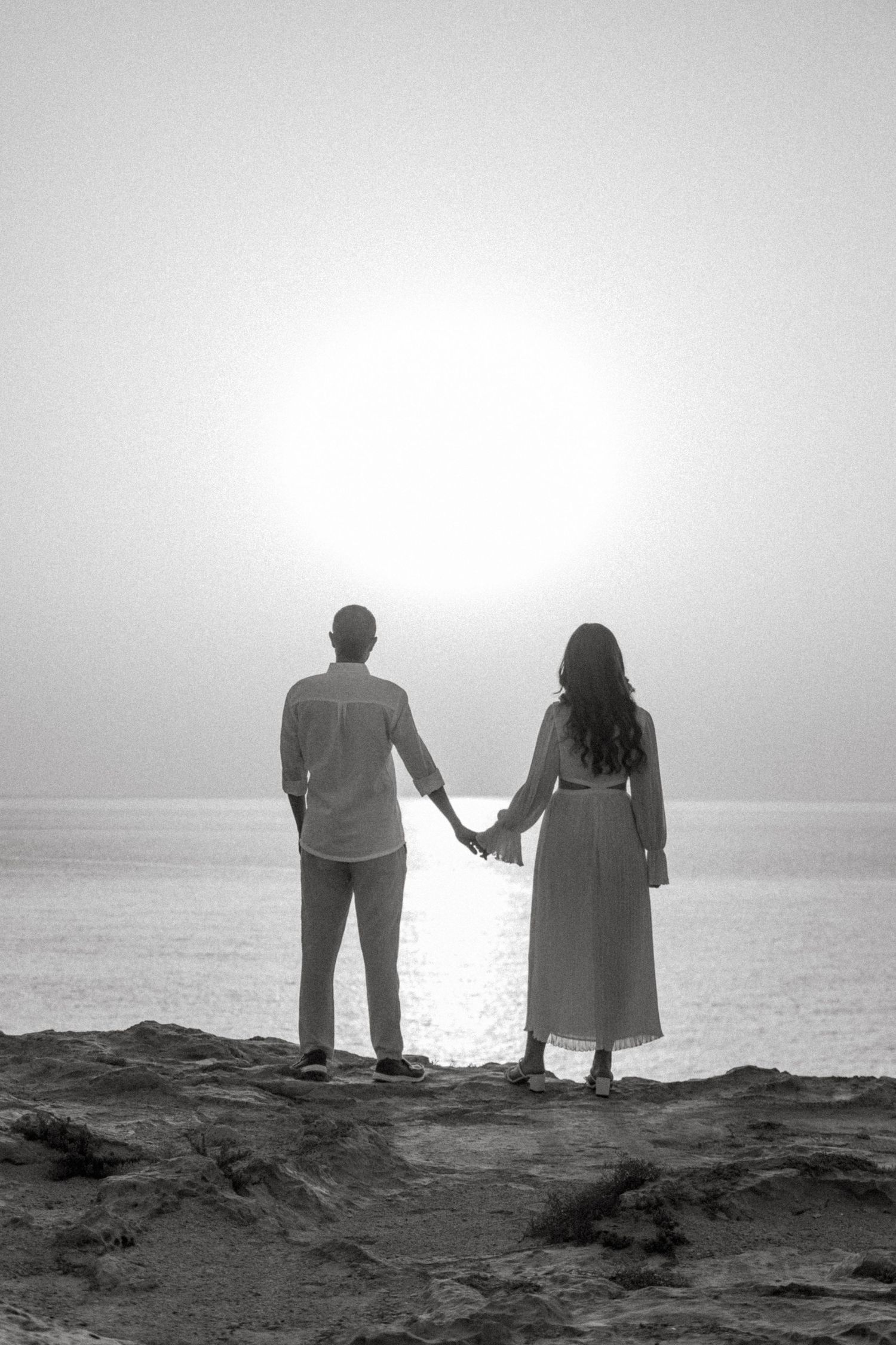 Silhouettes of a couple stand together against an ocean backdrop at sunset.