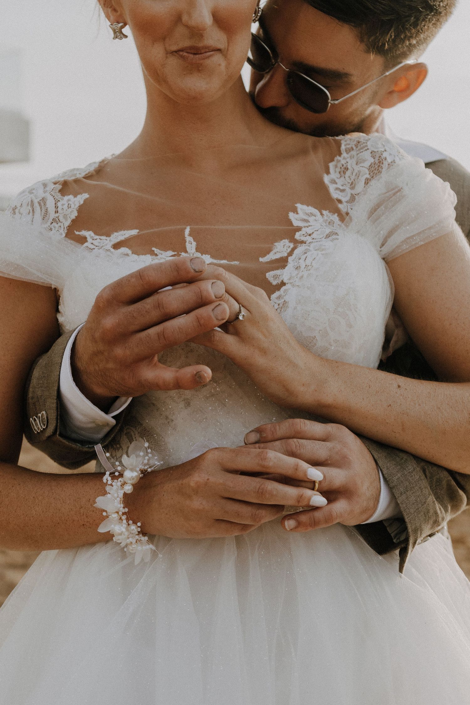 Close-up of wedding rings and lace dress details as couple embraces.