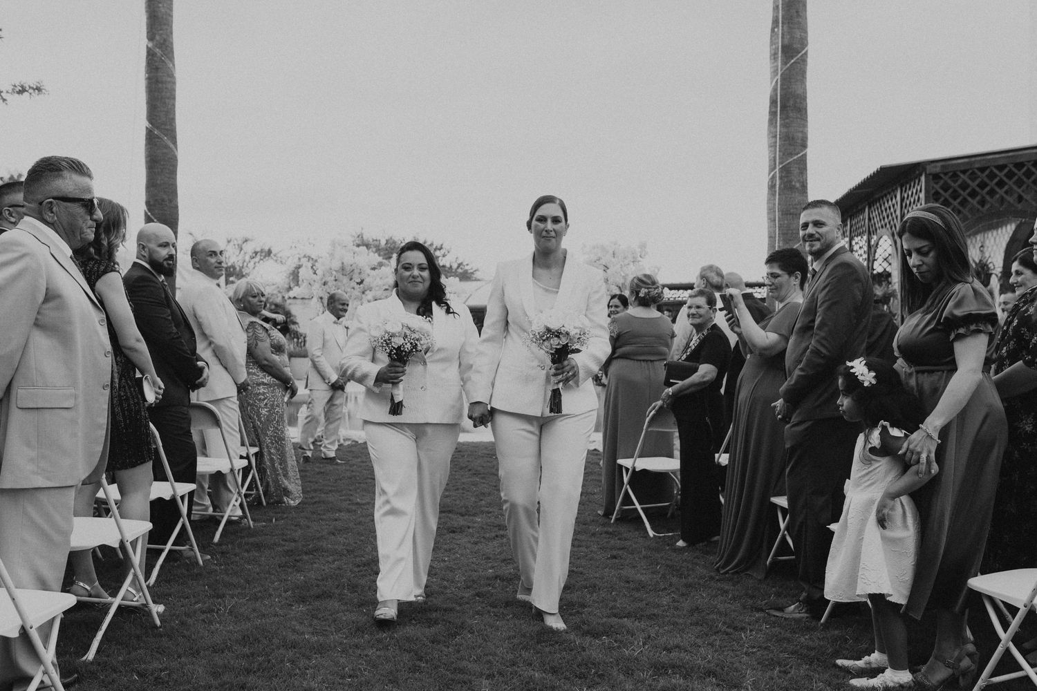 Wedding ceremony guests seated in white chairs on an outdoor lawn.