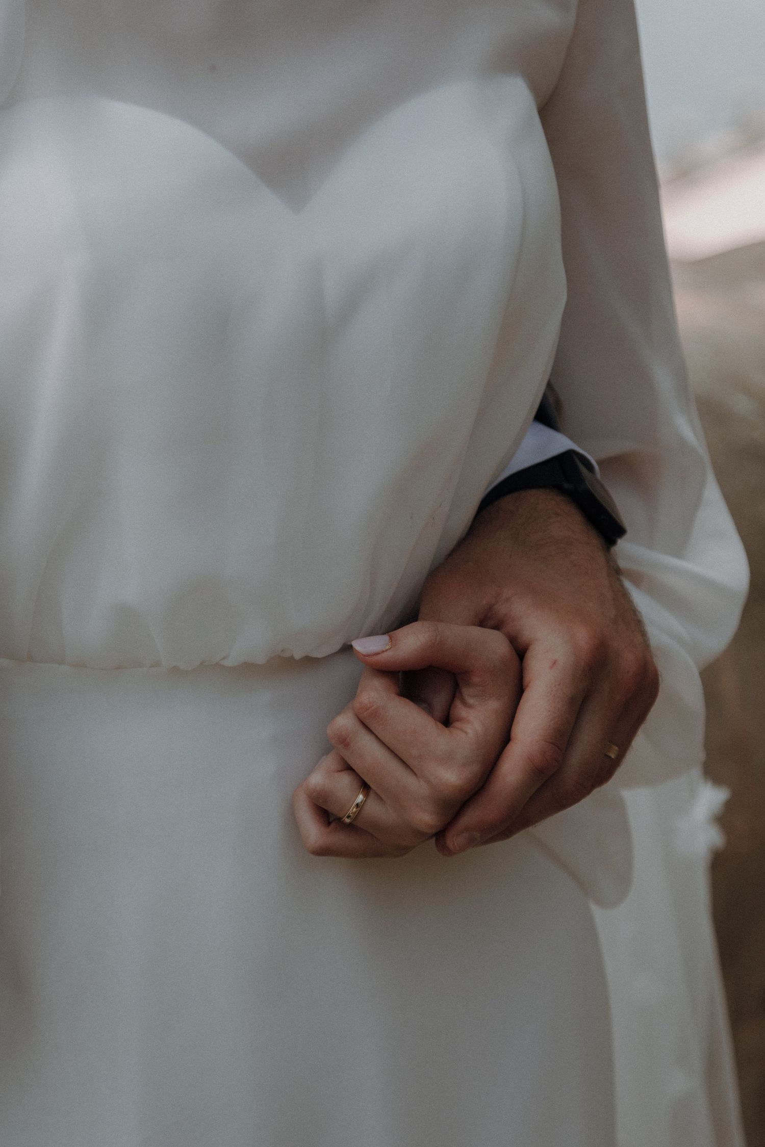 Close-up detail of hands and wedding ring against a white wedding dress.