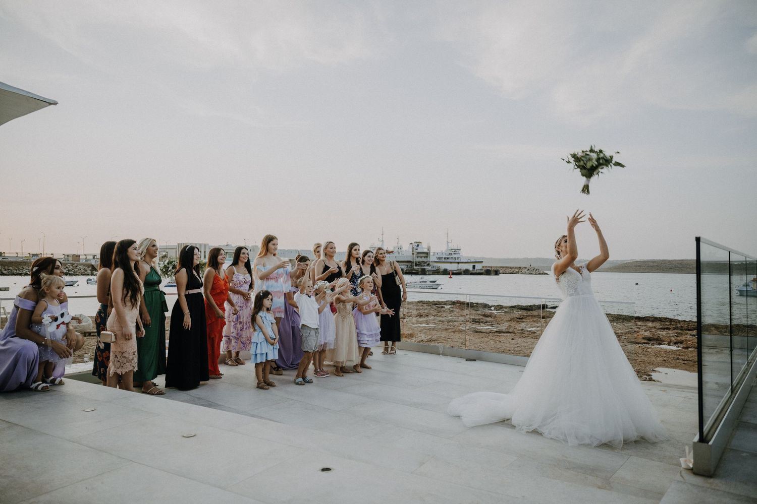 Wedding guests watch as the bride tosses her bouquet during an oceanside celebration.