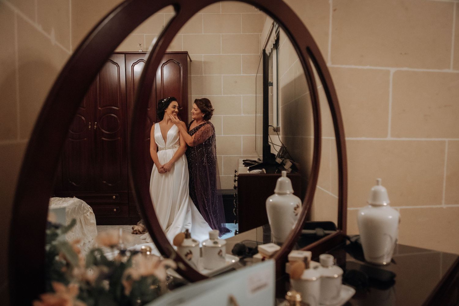 A reflection in an arched mirror shows wedding preparations in an elegant room.