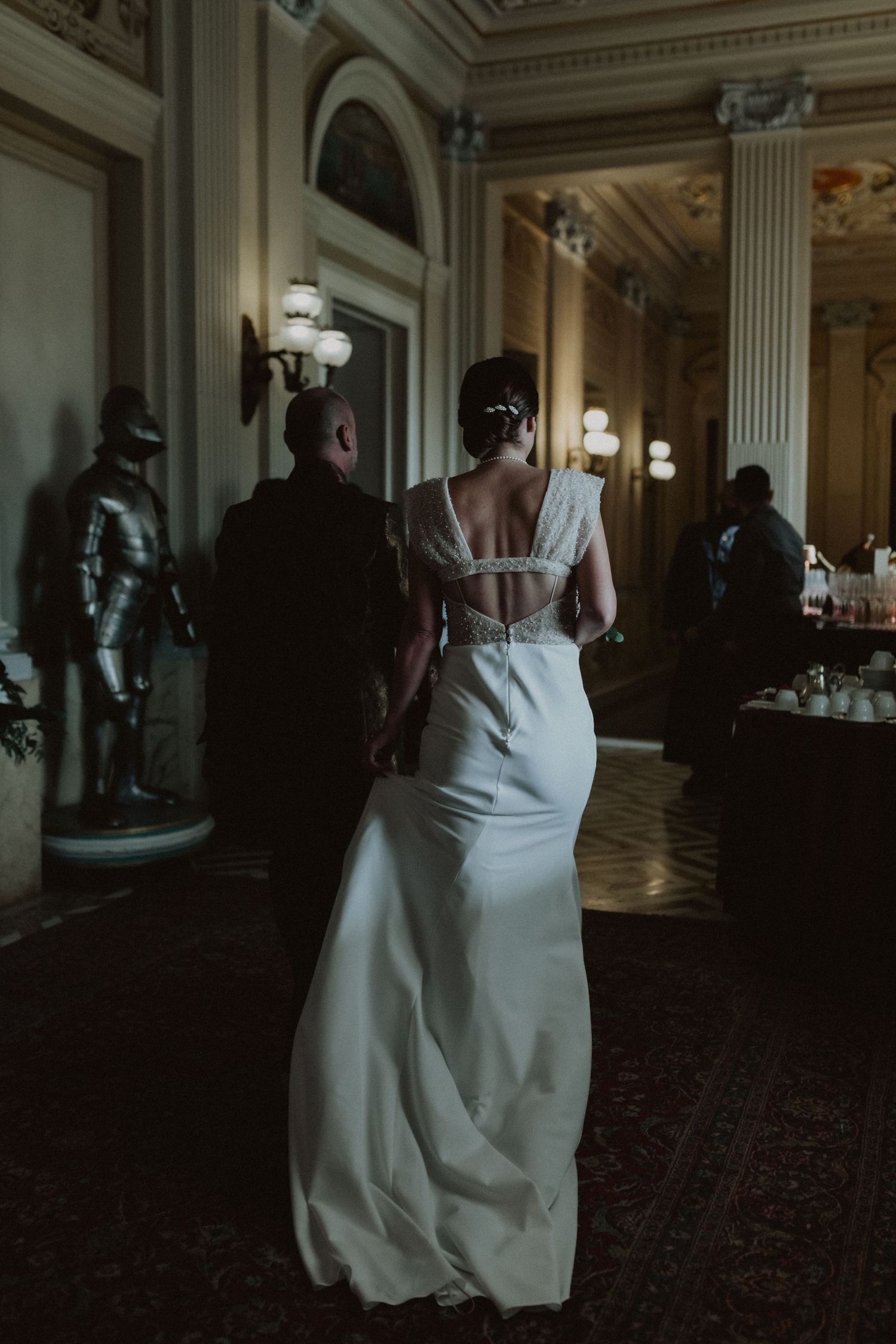 Elegant bride in a fitted white wedding gown walking through an ornate vintage hallway.