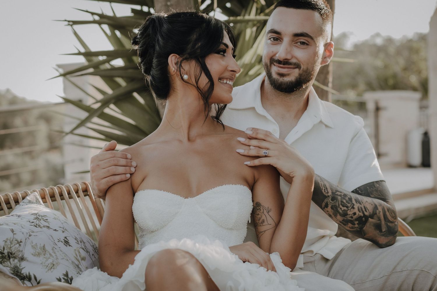 Romantic wedding couple relaxing on outdoor furniture during sunset photoshoot.