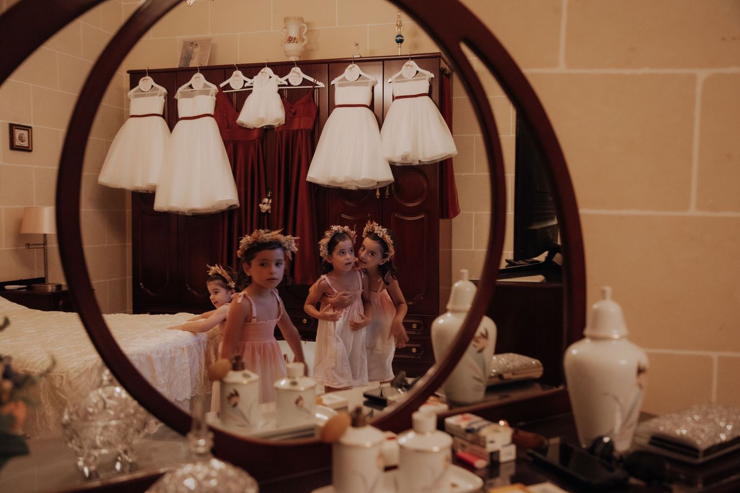 White flower girl dresses displayed on hangers against a dark wooden wall.