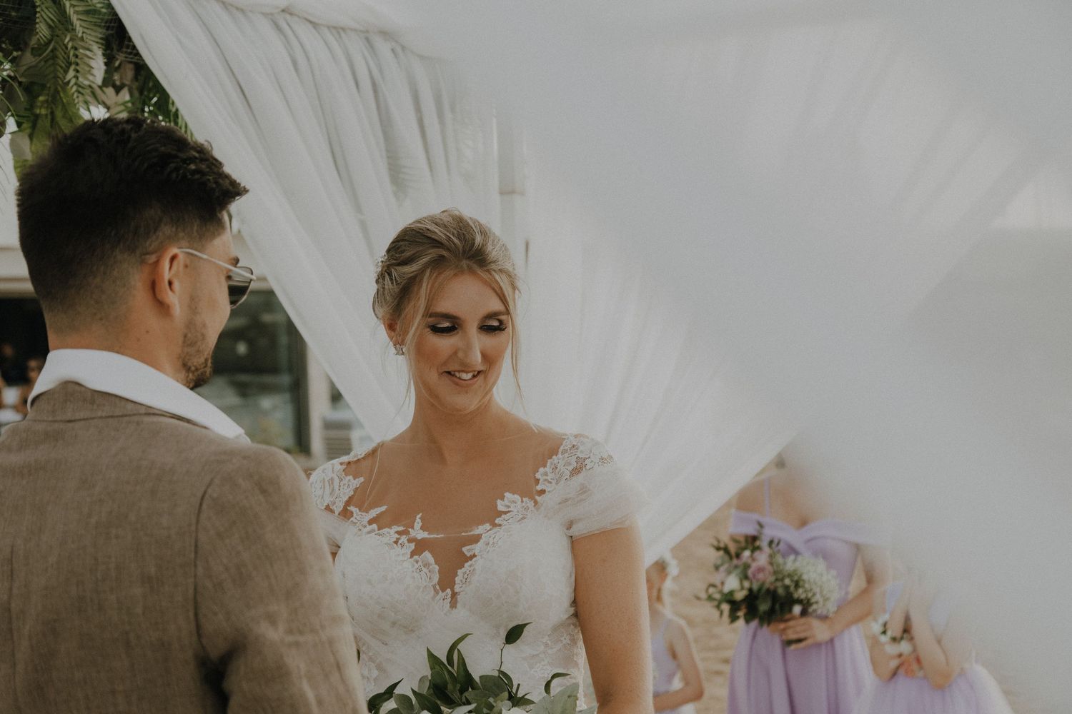 Intimate wedding ceremony moment under white draped canopy with beach backdrop.