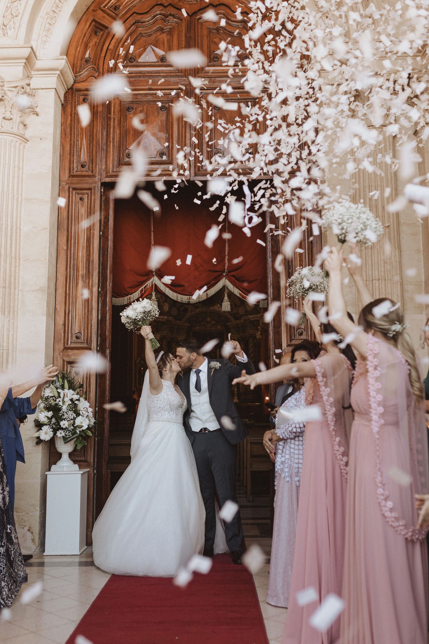 Wedding party celebrating with flower petals outside grand church doors.