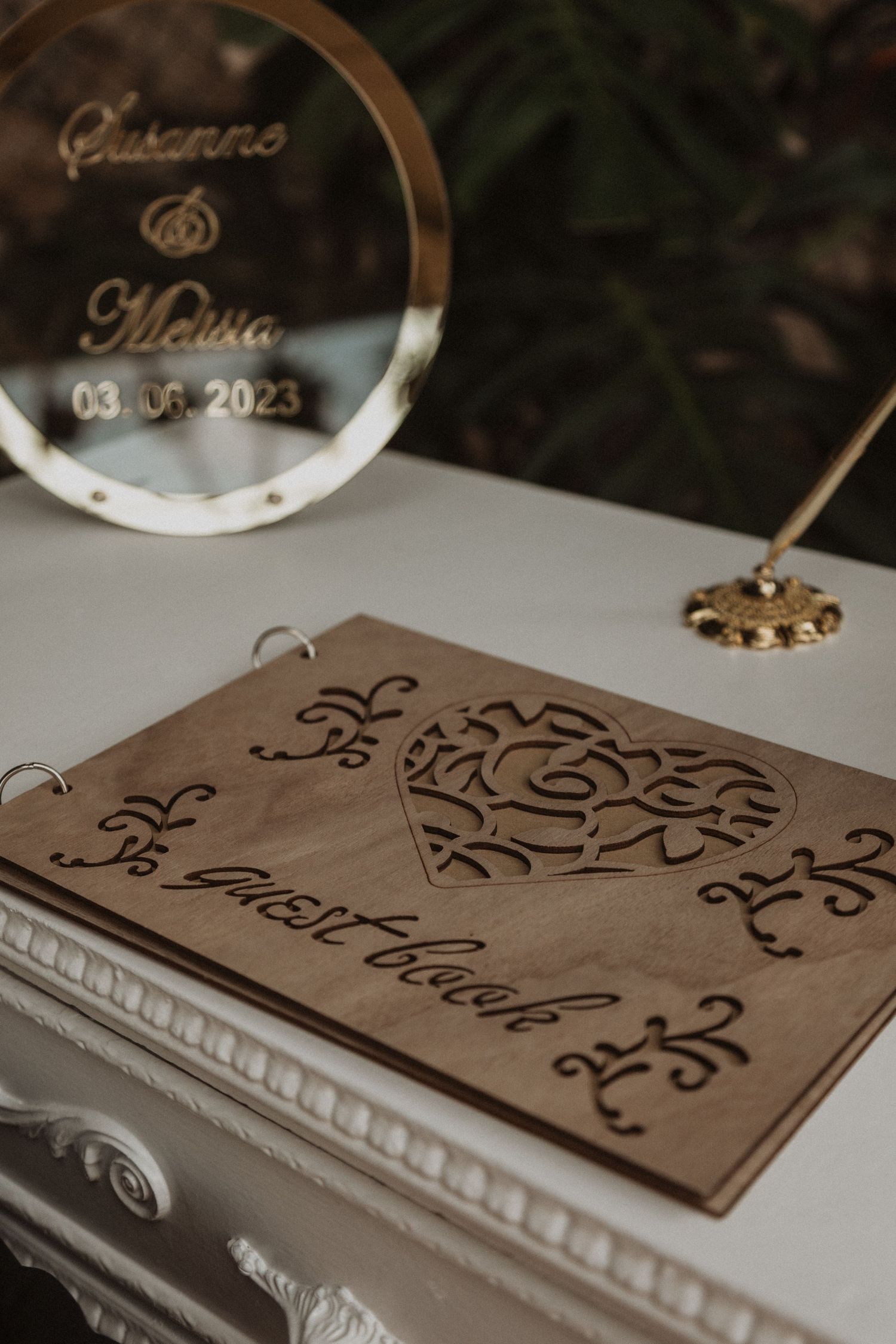 Wedding guest book with wooden cover featuring ornate heart design and couple's names.