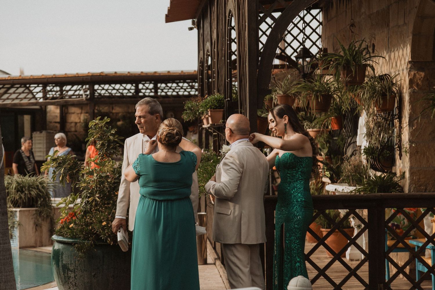 Wedding guests gathered under latticed pergola at outdoor reception venue.