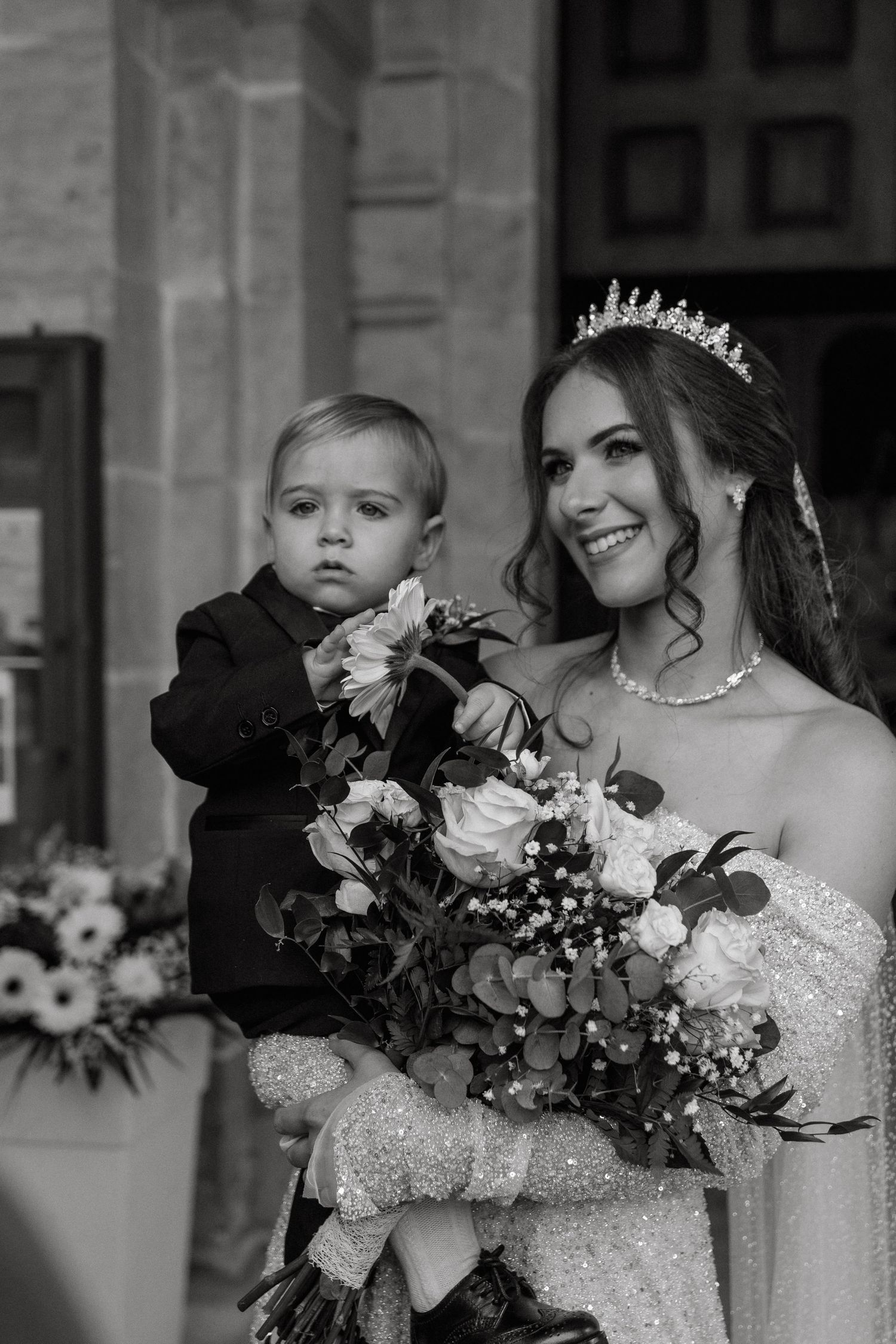 Black and white portrait of bride in sparkling gown holding bouquet with small child.