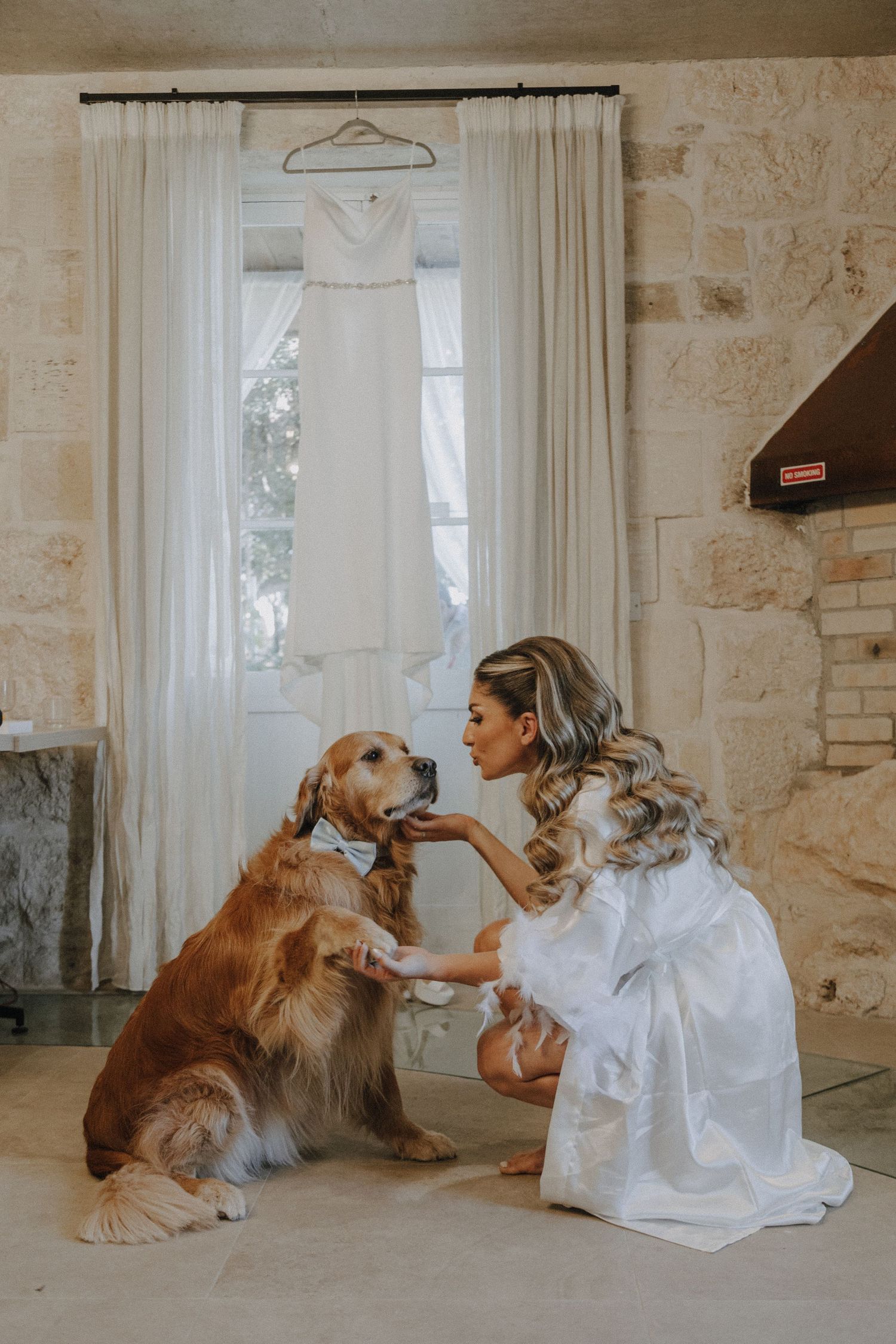 A bride in a white gown shares a tender moment with her golden retriever beside a hanging dress.