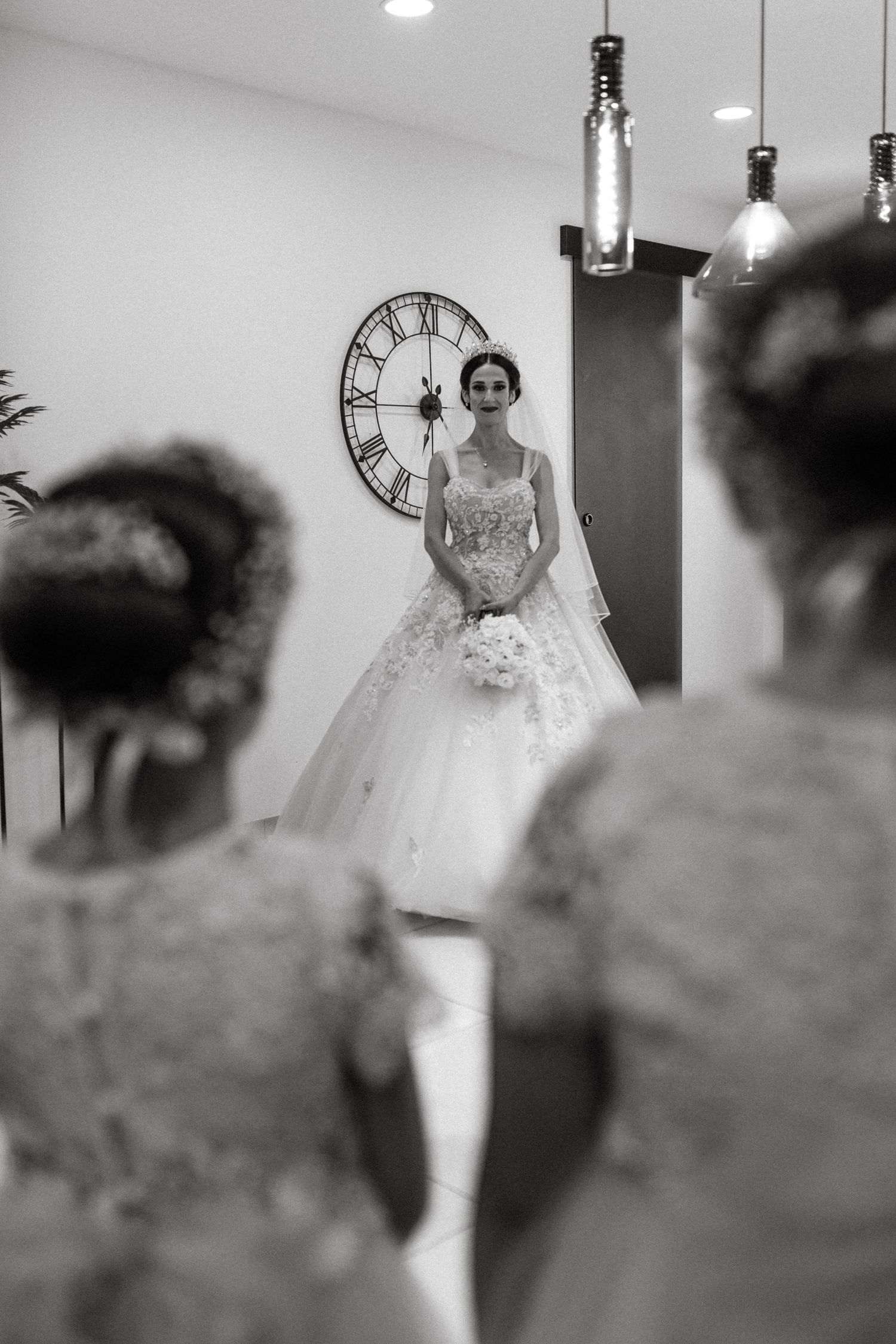 Bride in ornate ballgown poses in front of vintage clock during wedding preparations.