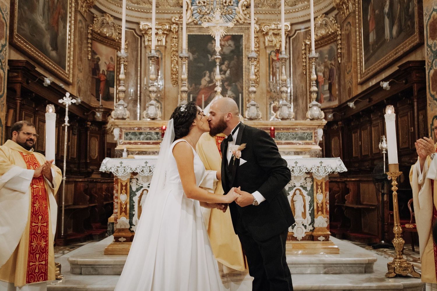 A couple shares their first kiss during a wedding ceremony in an ornate church altar.