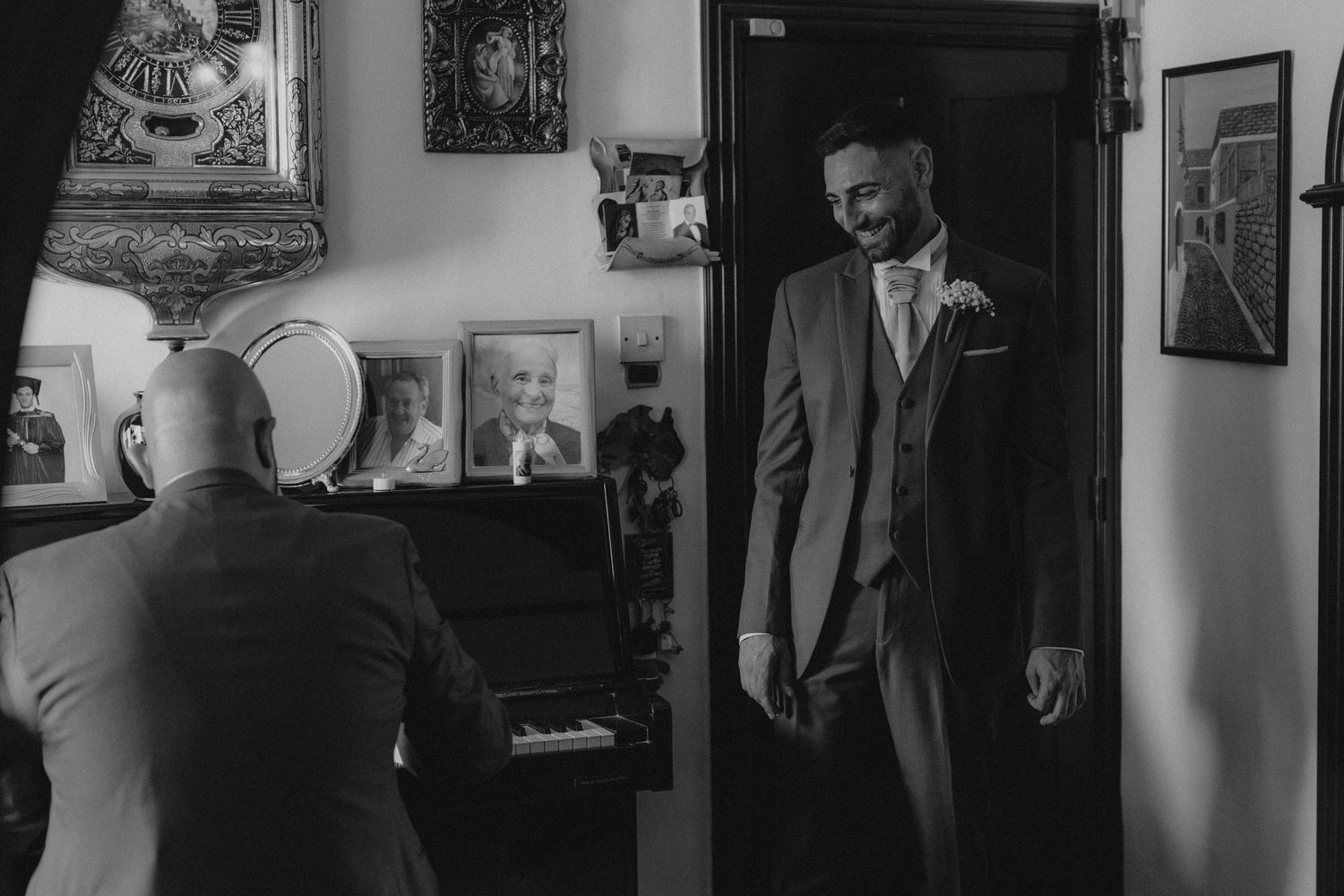 Black and white portrait of groom preparing in a room filled with framed artwork.