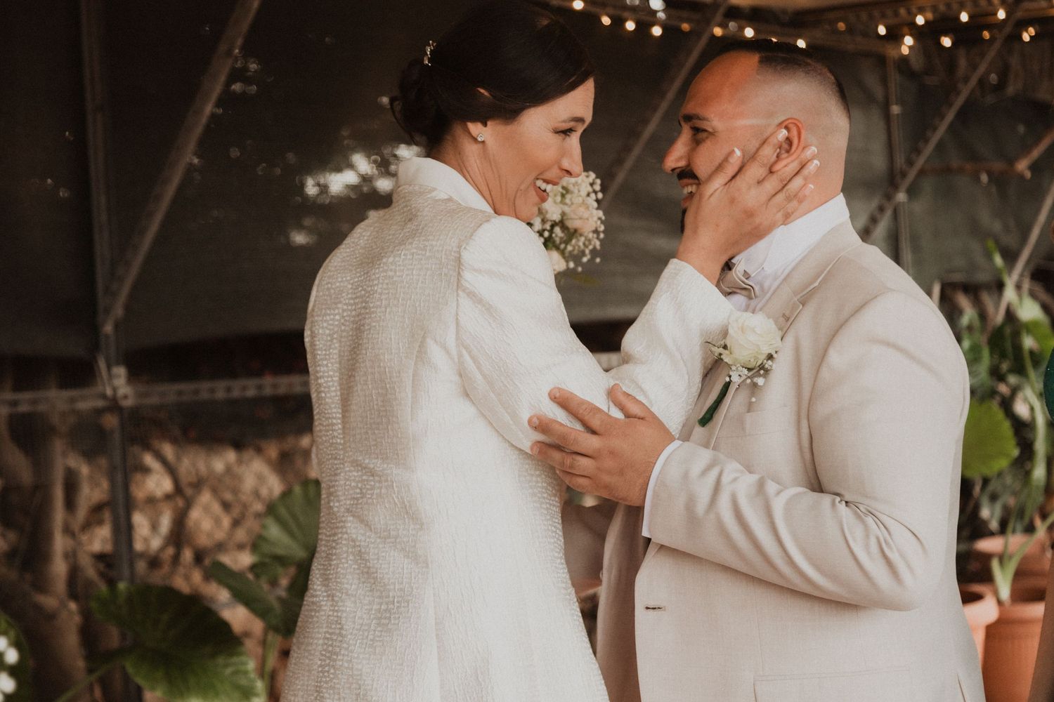 Intimate wedding ceremony moment with couple embracing in front of rustic wooden backdrop with twinkling lights.