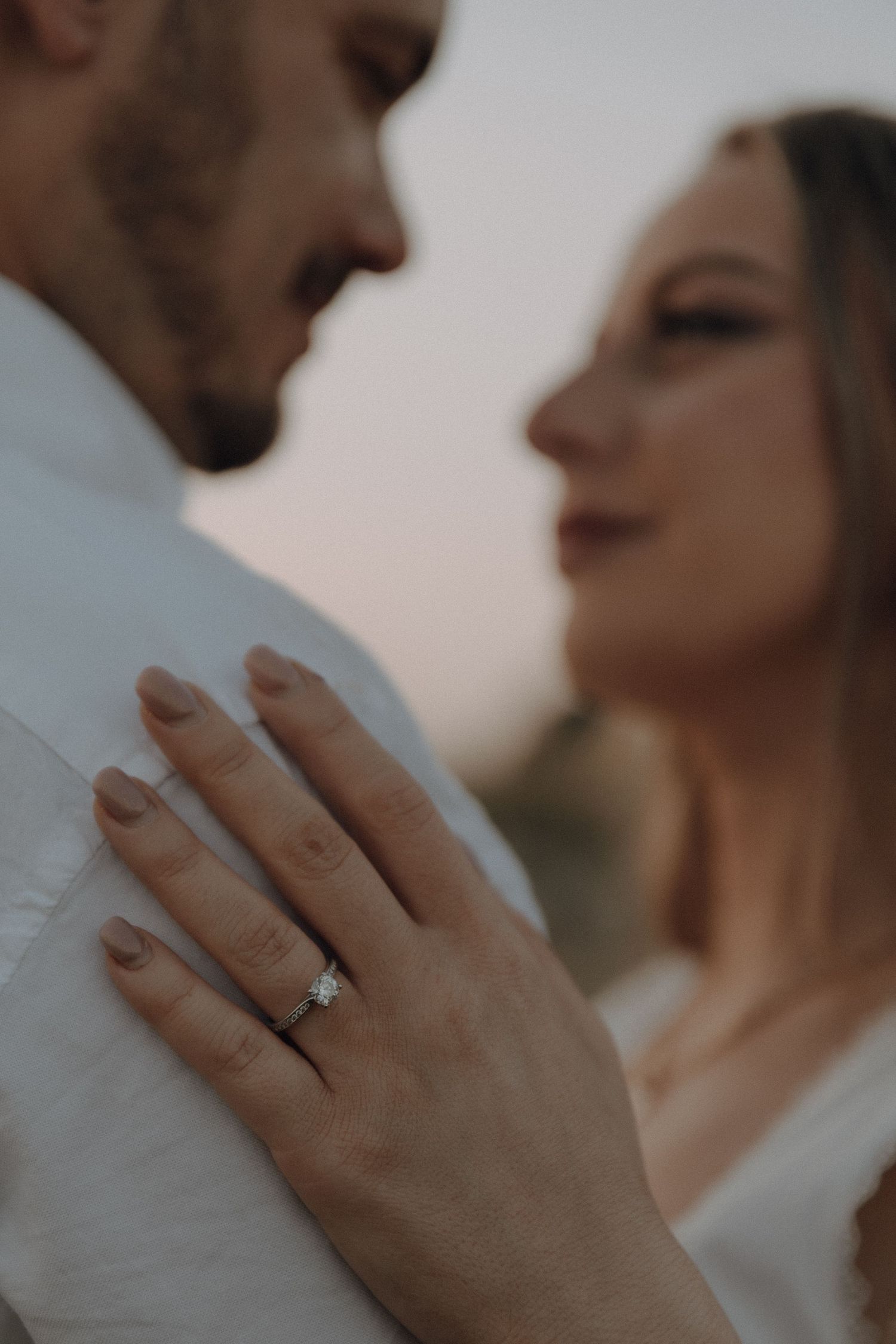Close-up of an engagement ring on a woman's hand as a couple shares an intimate moment outdoors.