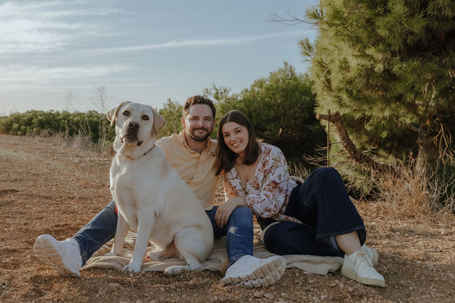 A group of people and dogs sitting together outdoors during a golden hour photoshoot in a natural setting.