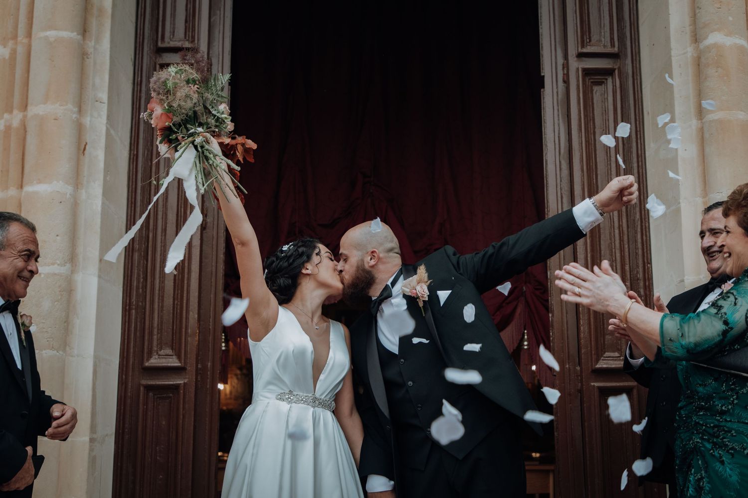 Newlyweds exit church doors as guests shower them with flower petals during a joyous wedding celebration.