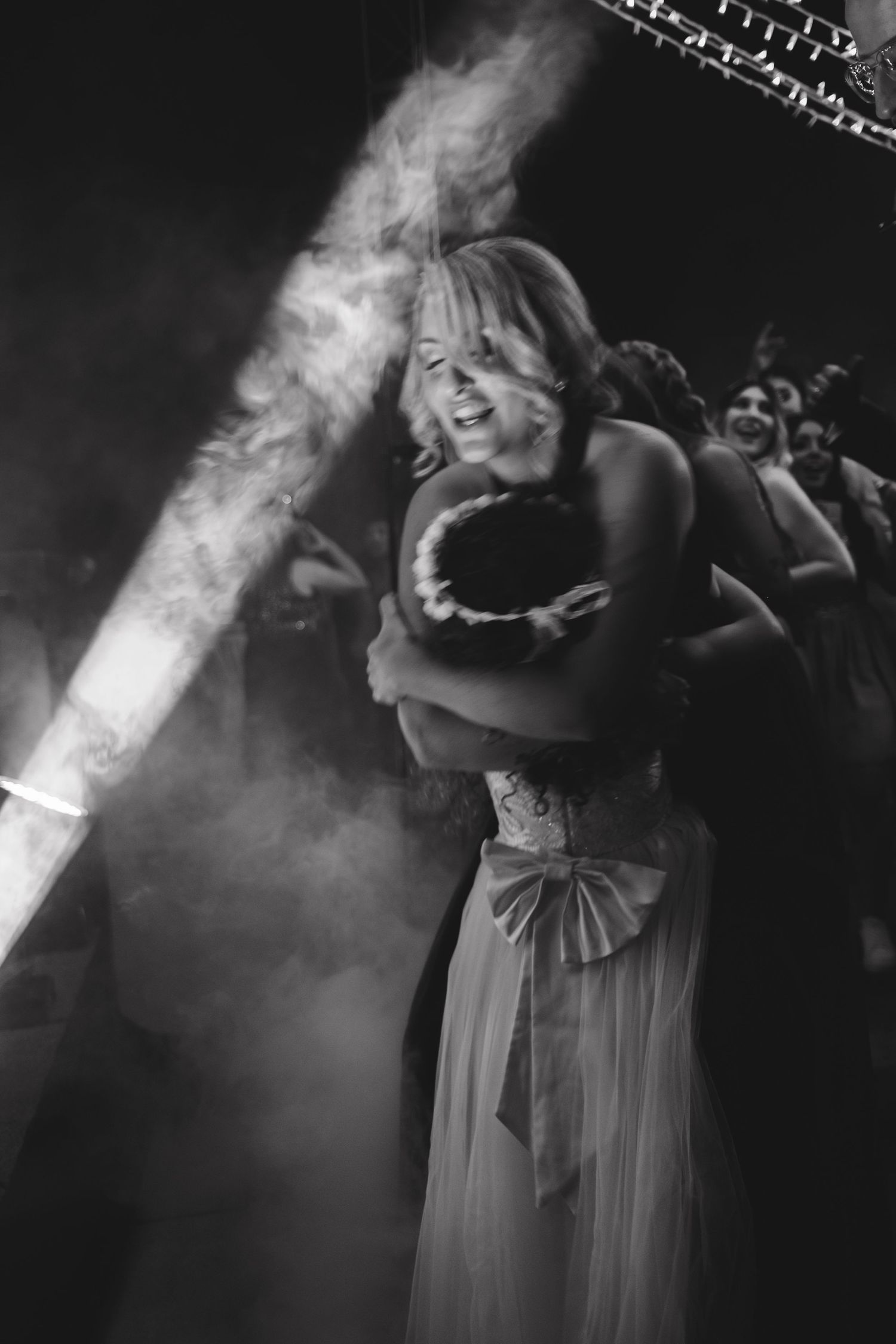 Couples dancing in dramatic lighting with fog effects at wedding reception.