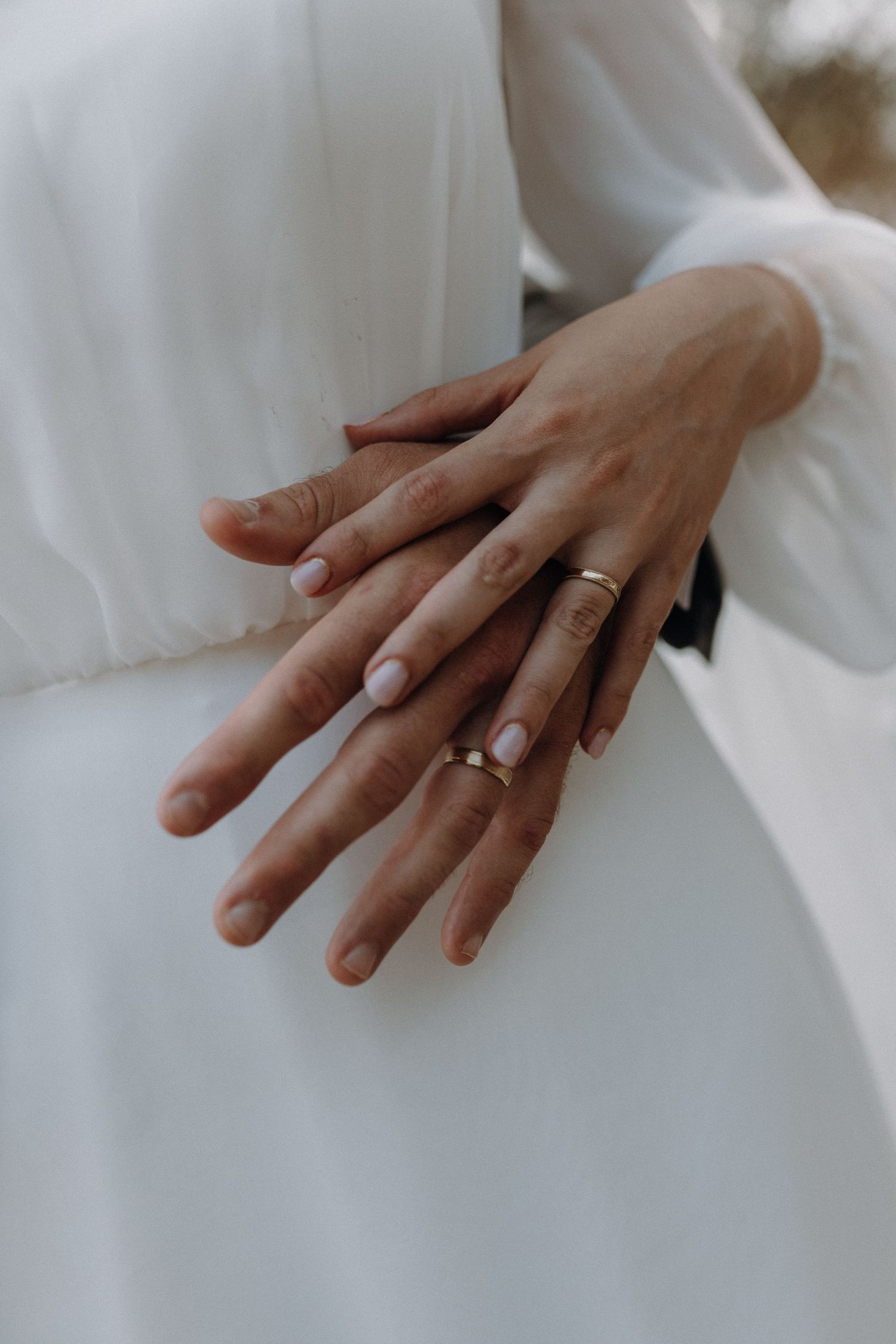 Close-up detail shots of hands wearing wedding rings against white fabric.