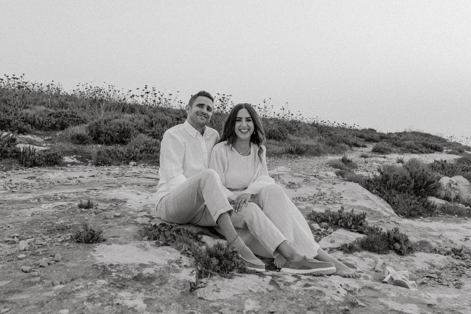 A black and white photo captures a couple's romantic moment on rocky terrain.