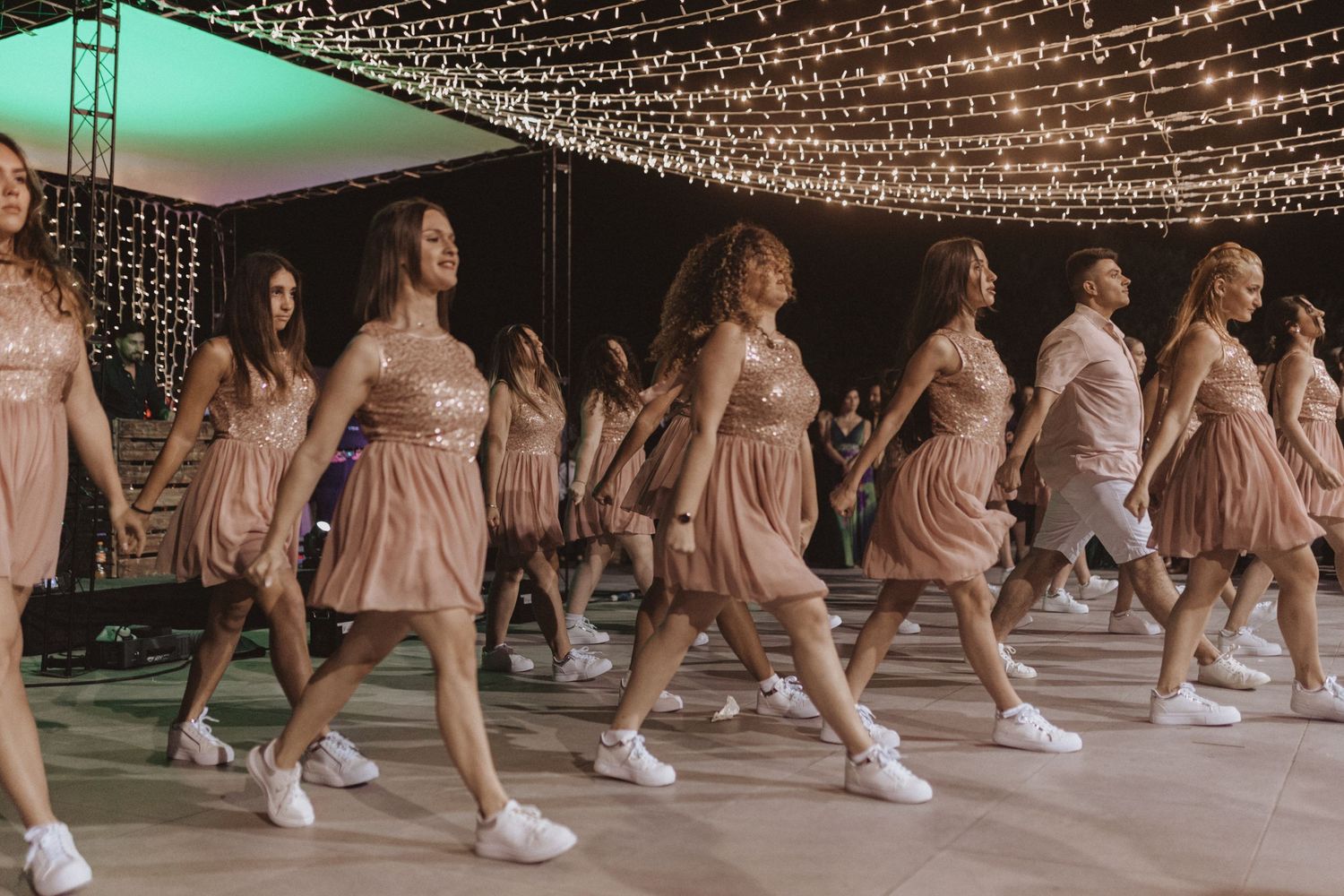 Dancers in coordinated pink outfits performing a choreographed routine under twinkling lights.