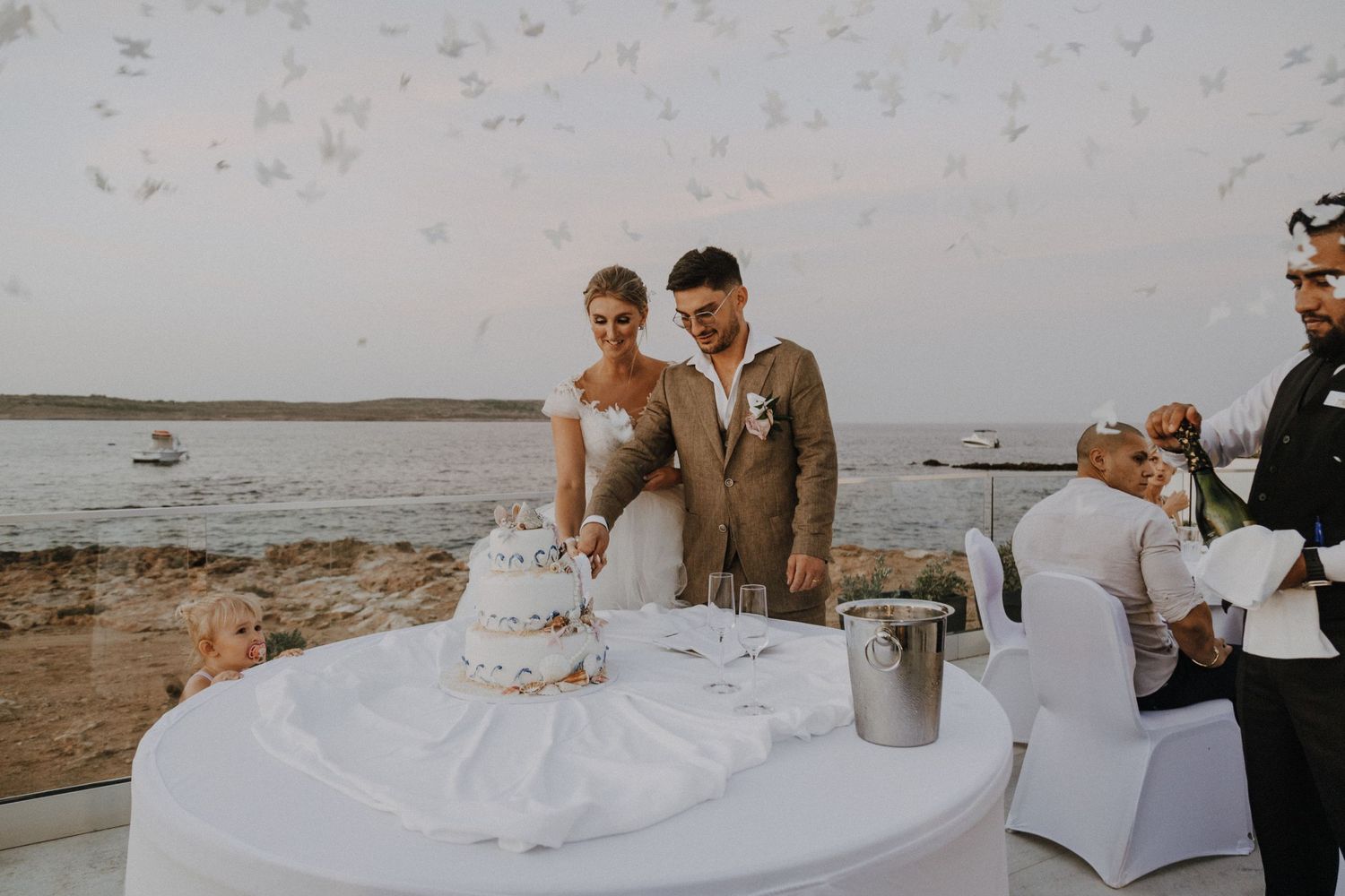 Wedding party enjoying cake cutting ceremony at waterfront venue.