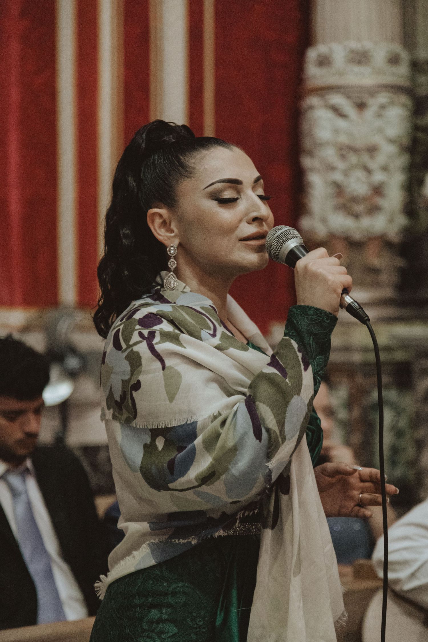Wedding singer in camouflage jacket and emerald dress performs at ornate venue.