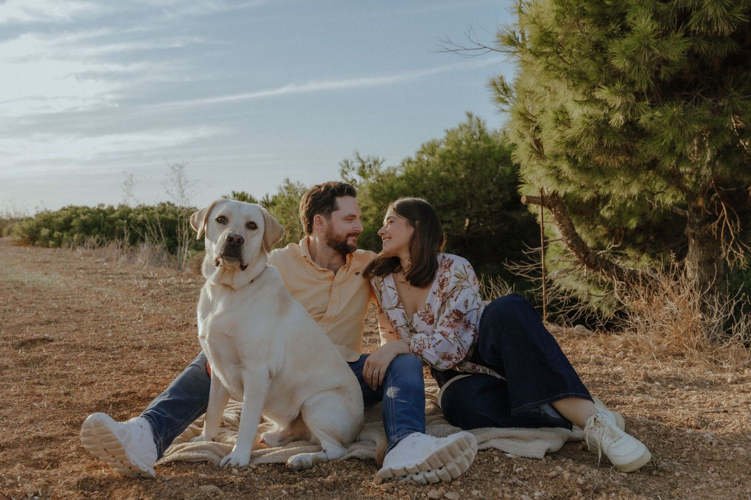 Couple having a romantic picnic outdoors with their large white dog on a sunny day.