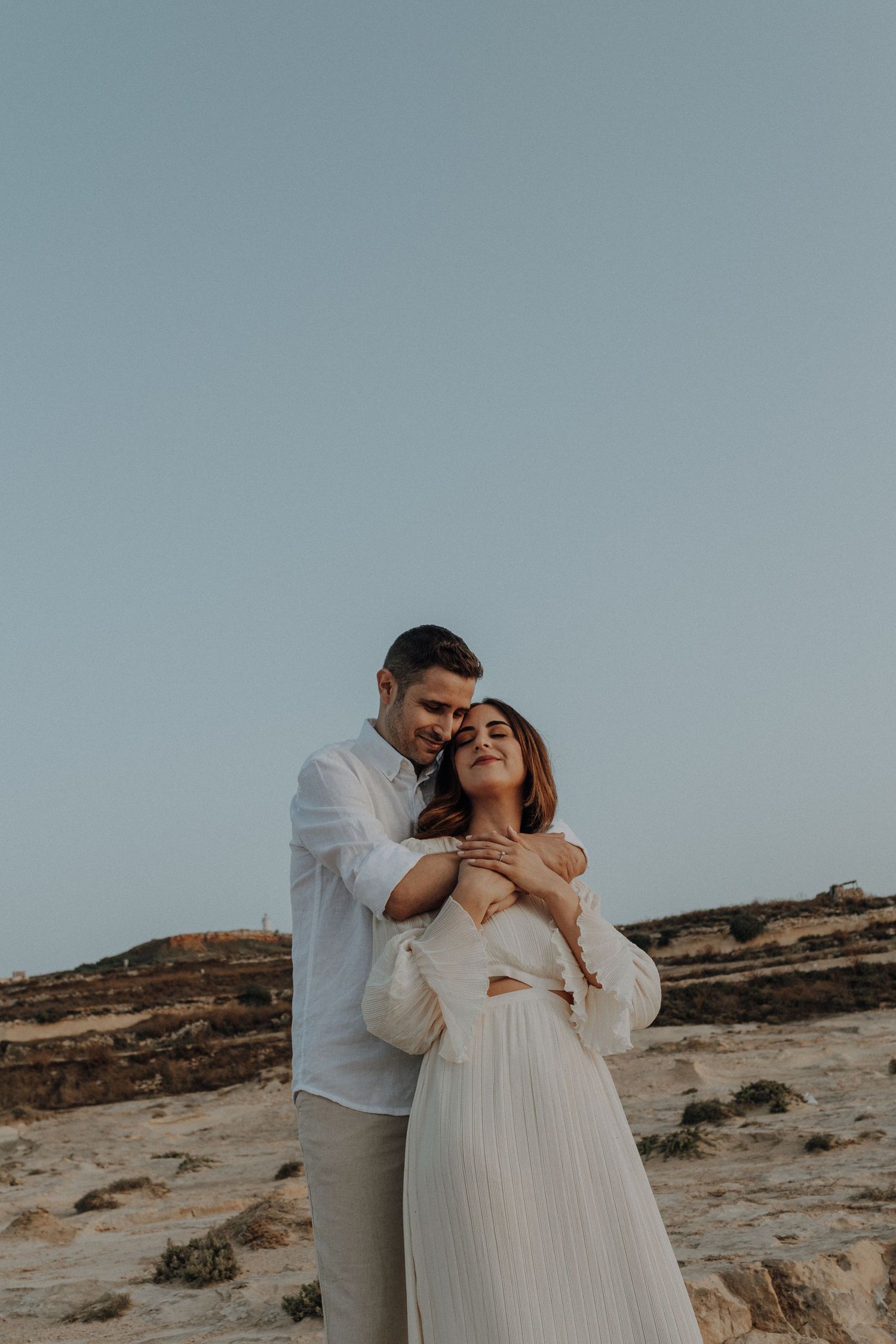 An intimate photoshoot of a couple embracing on a coastal cliff.