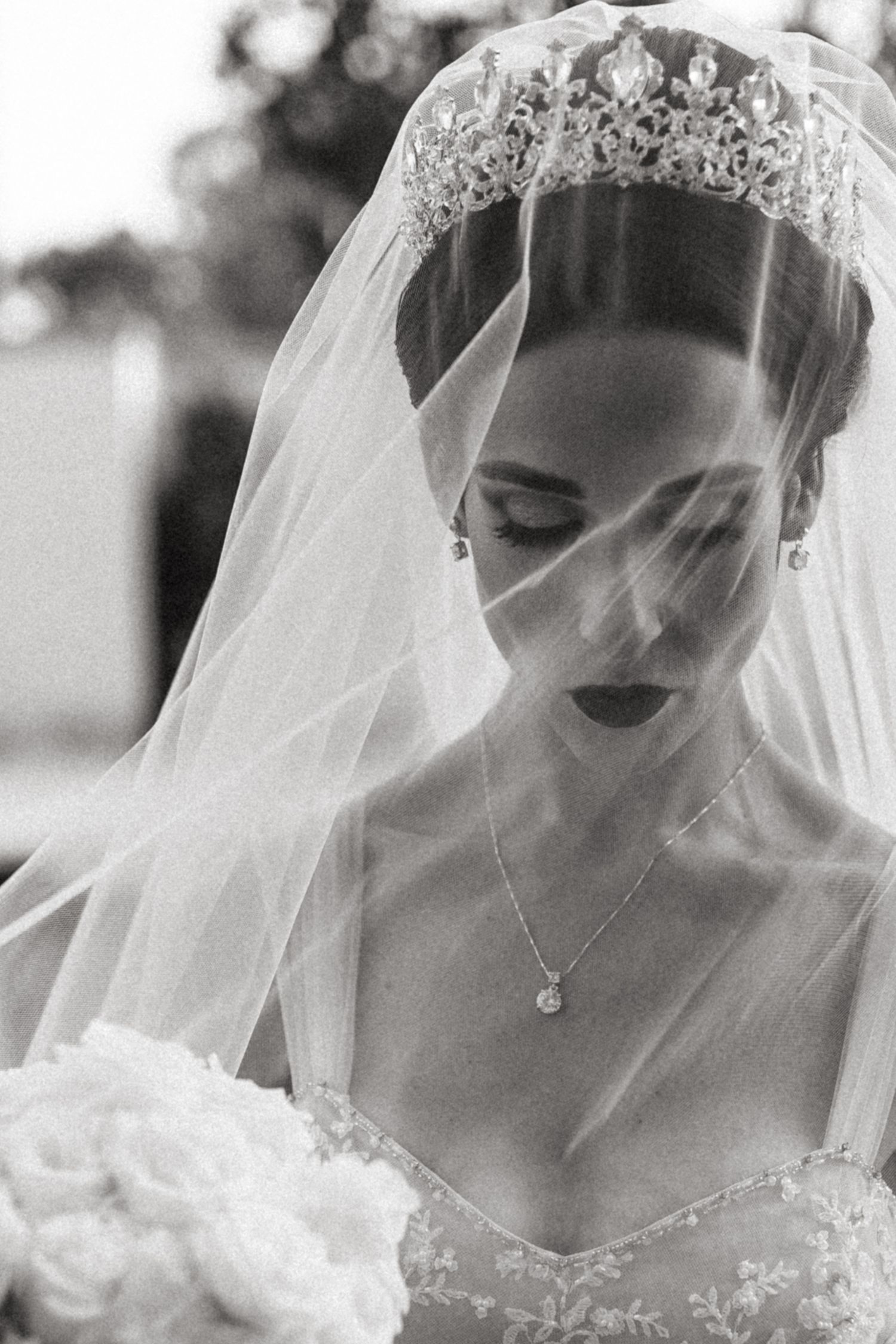 Dramatic black and white closeup of veiled bride wearing tiara and delicate necklace.