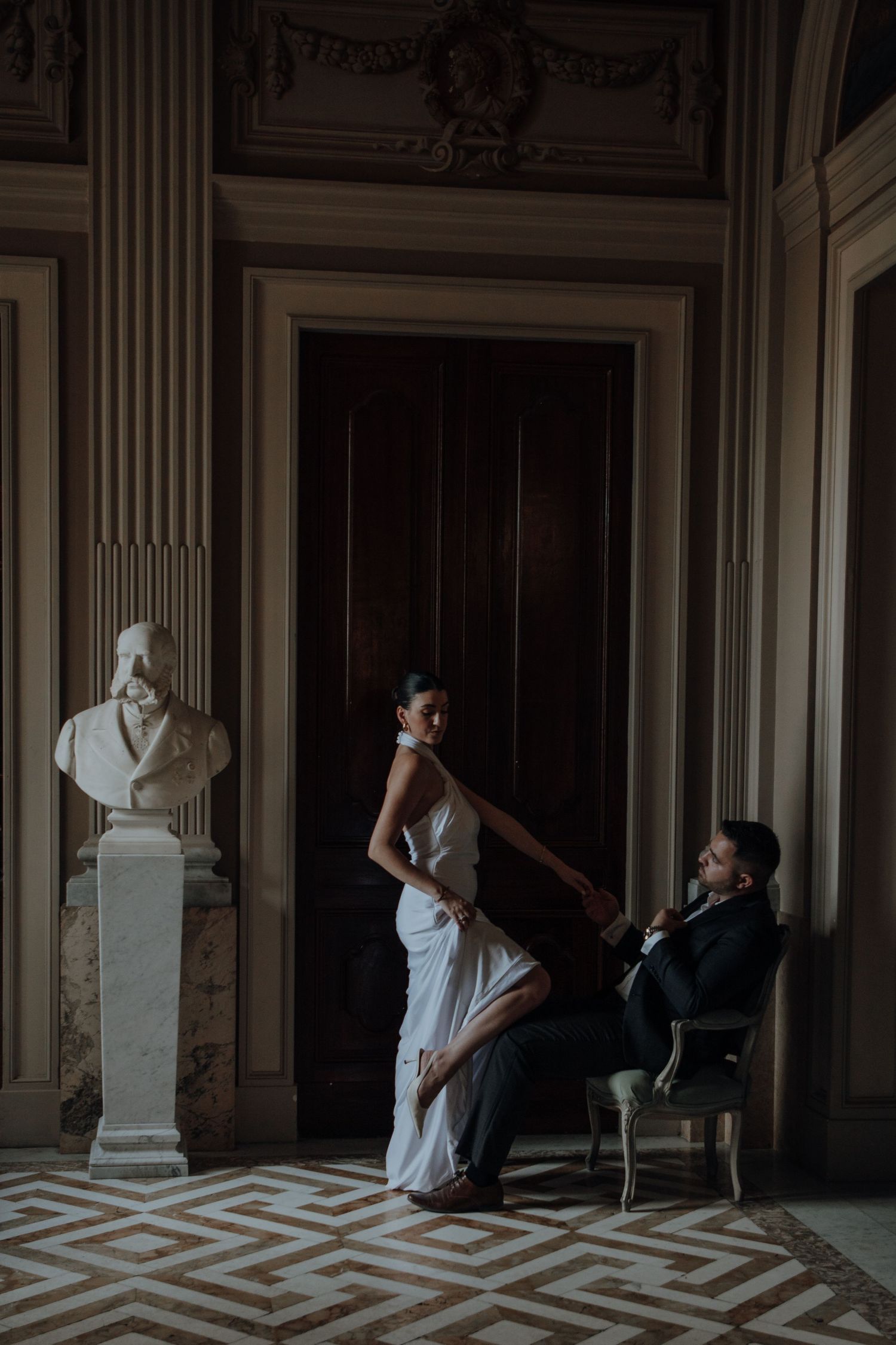 Couple in formal attire lounging on floor of grand room with geometric patterned floor.