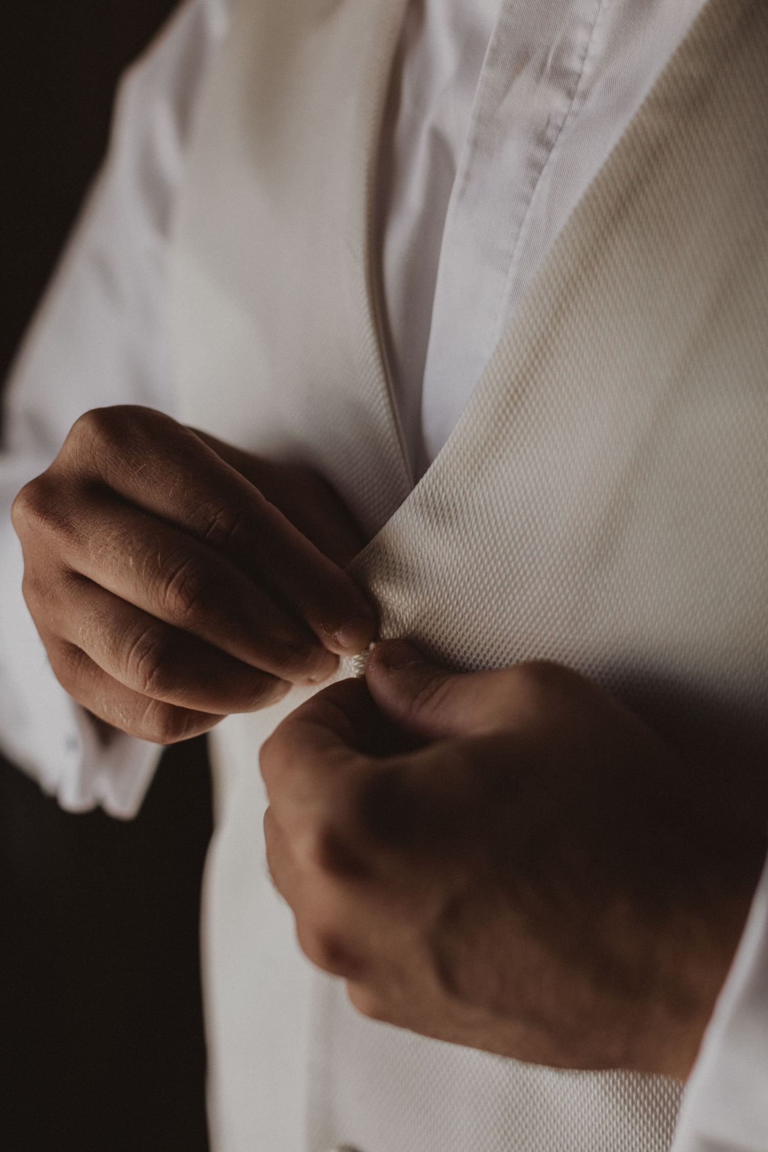 Close-up of hands buttoning a crisp white dress shirt.