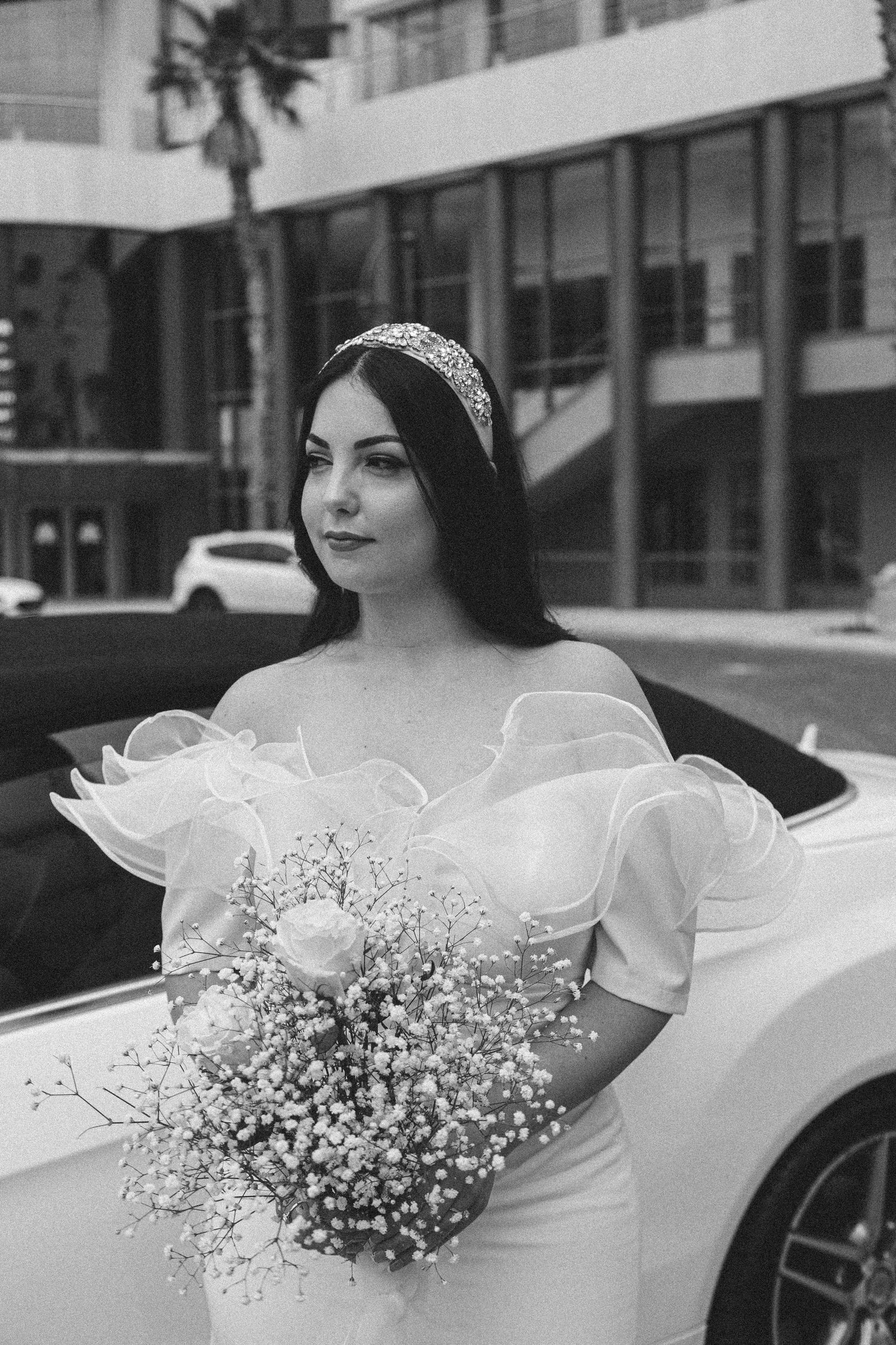 Black and white portrait against a luxury car with bridal bouquet.