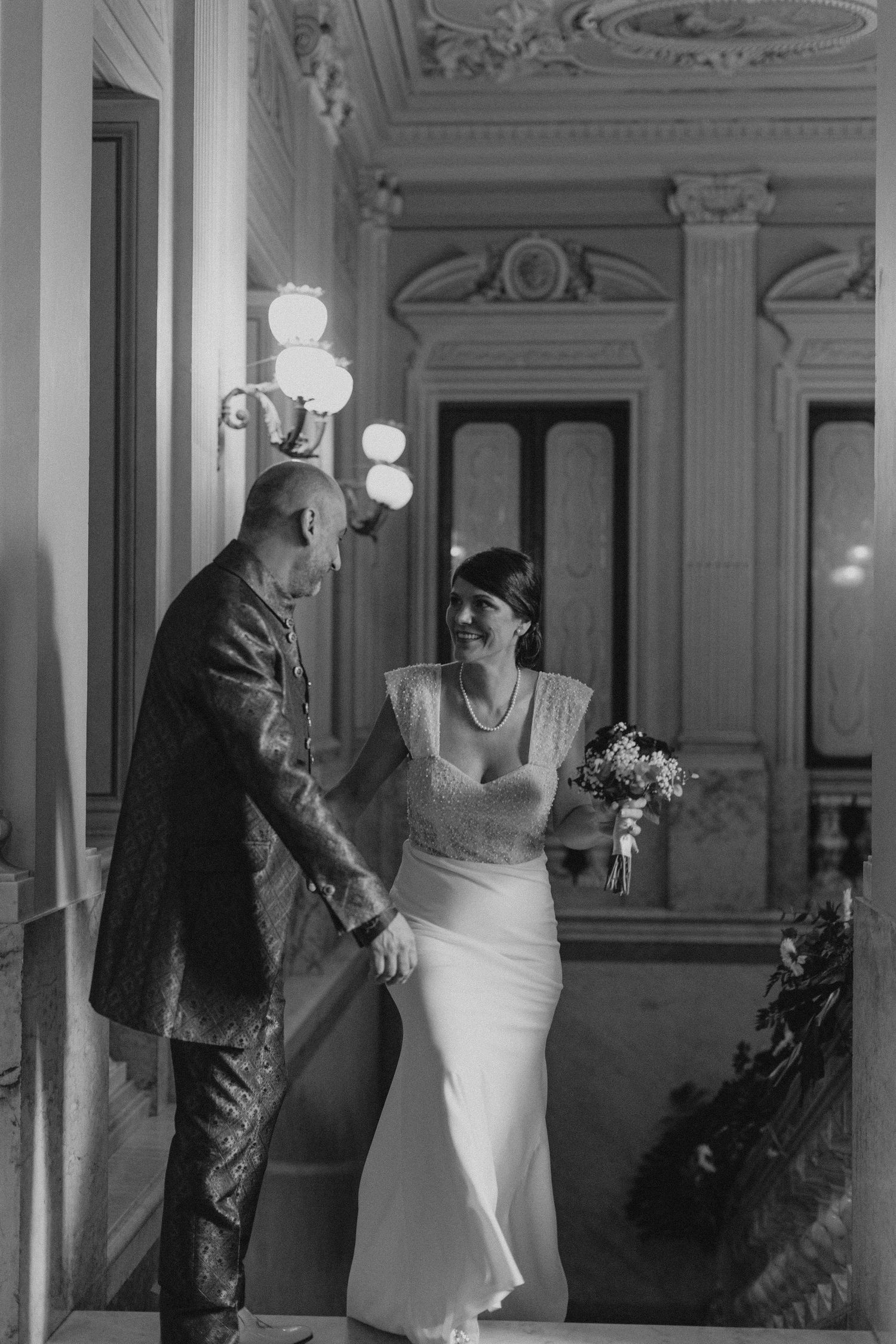Black and white photo of a couple sharing a moment in an elegant hallway.